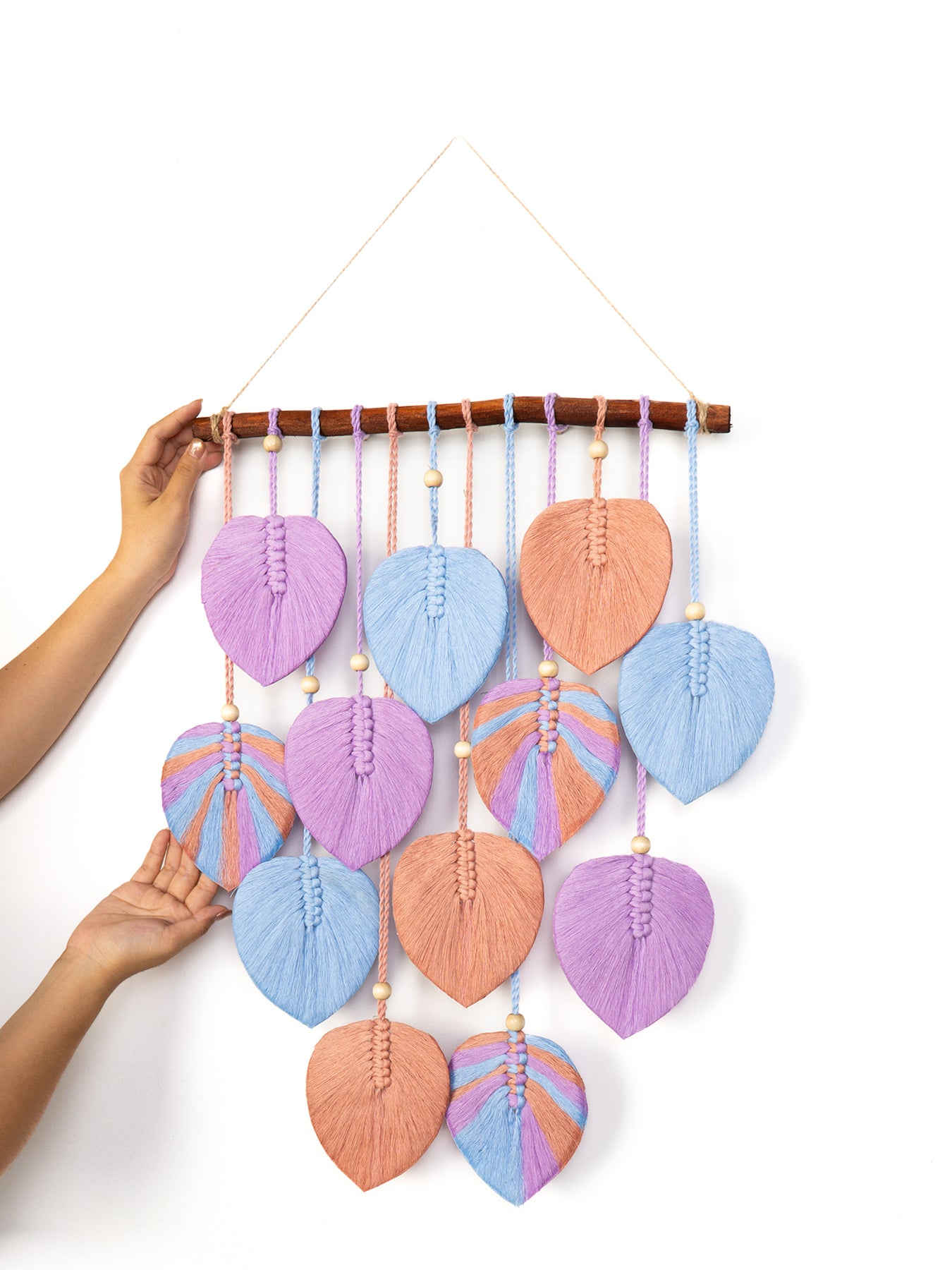 Handmade wall hanging with green leaf-shaped fabric pieces and wooden branch on a white background