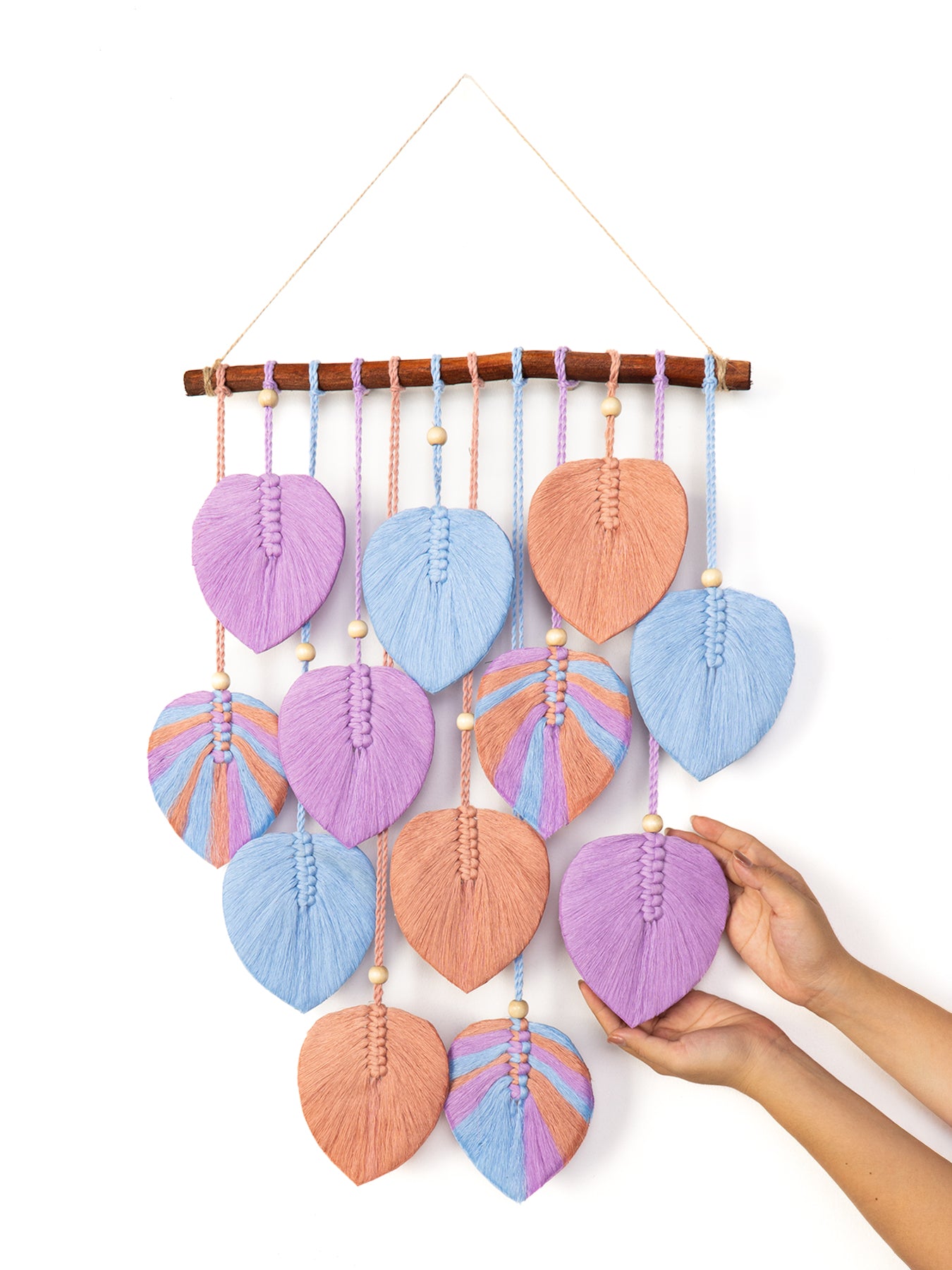 Handmade wall hanging with leaf-shaped green fabric pieces and wooden branch on a white background