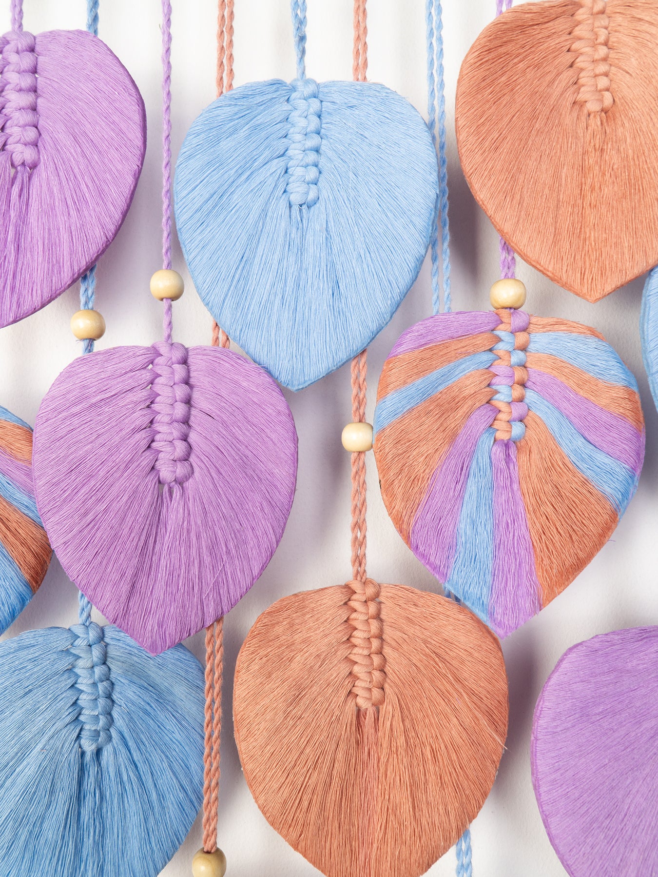 Green leaf-shaped macrame decorations with wooden beads on a white background