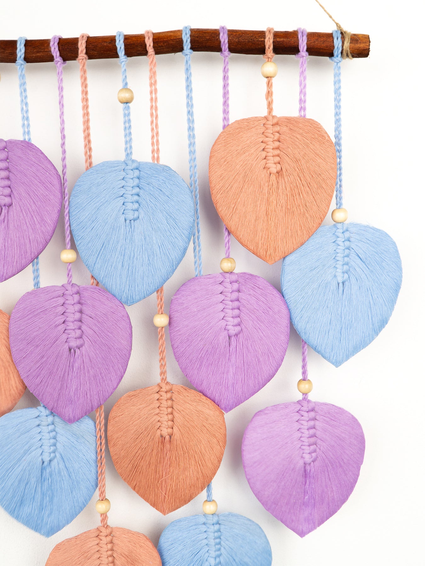 Colorful yarn leaf decorations hanging from a branch on a white background