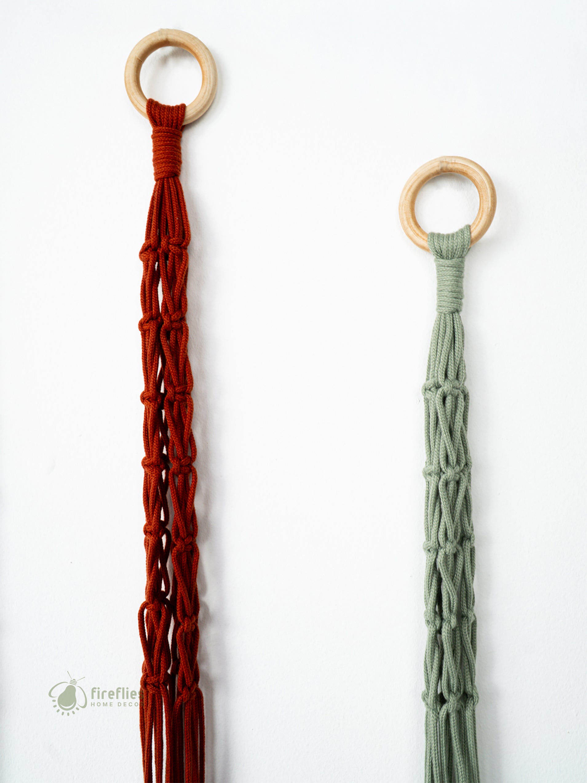 Two macrame plant hangers, one red and one green, with wooden rings on a white background.
