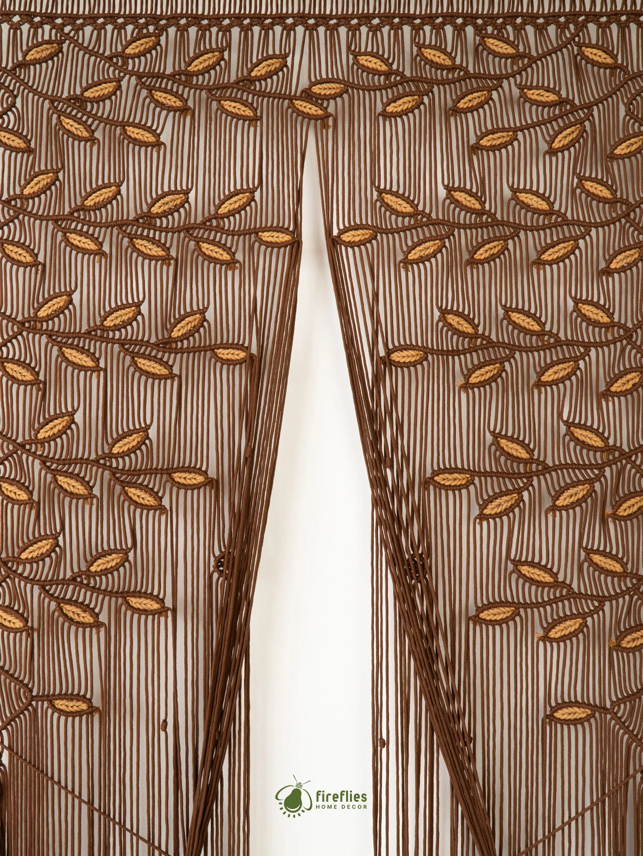 A brown sheer curtain panel with an embroidered leaf and vine pattern, hanging in front of a white window frame. The brand name 'fireflies home decor' is visible at the bottom center.