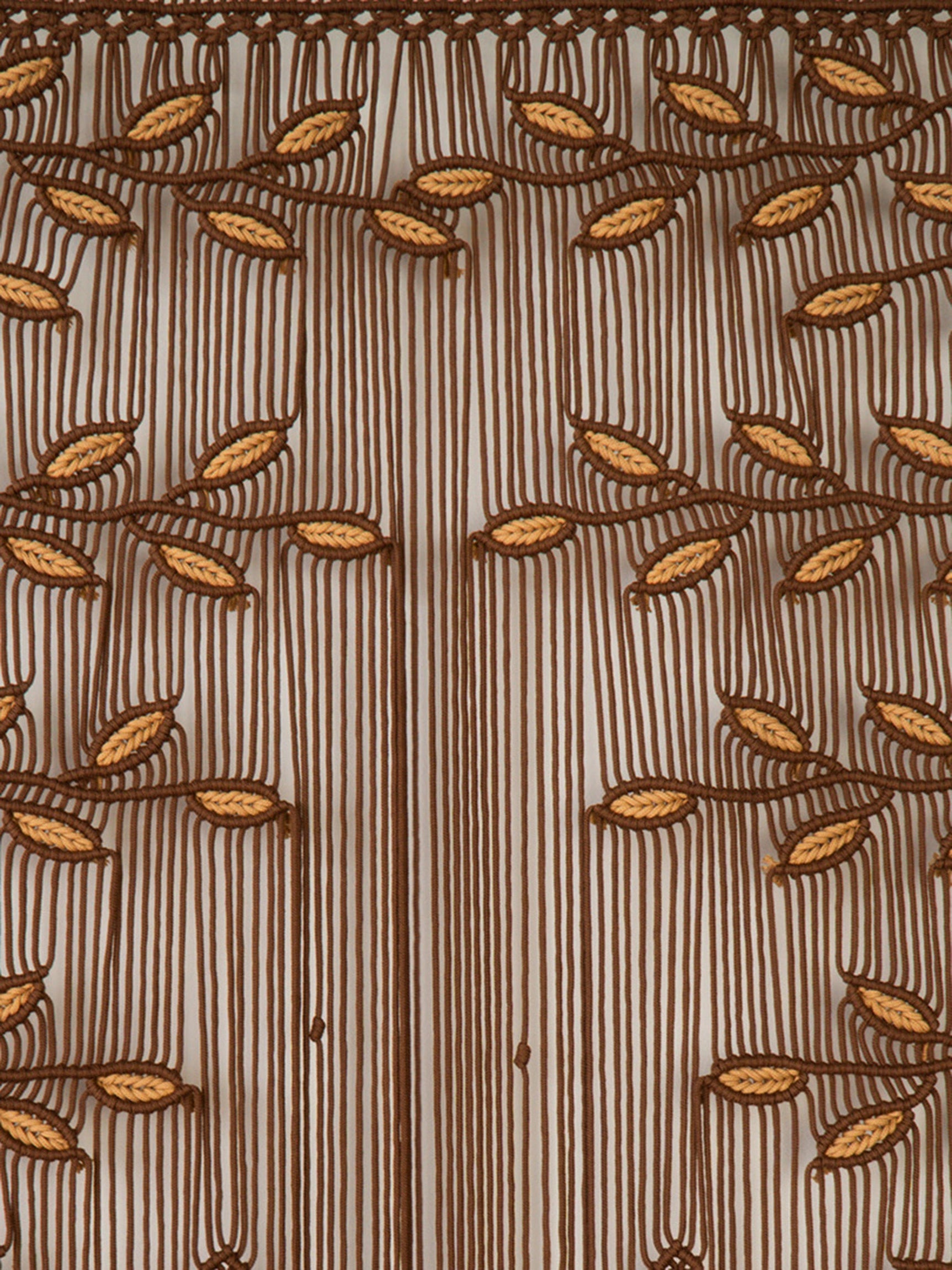 Close-up of a sheer brown curtain panel with vertical stripes and embroidered leaf motifs in warm brown and tan, shown hanging with fringe at the bottom.