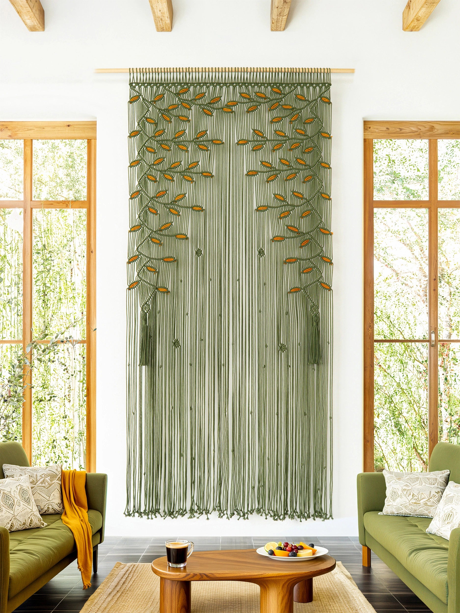 A long sheer curtain panel in sage green with embroidered leafy branches, hanging in a bright living room with wood-framed windows, green sofas, and a wooden coffee table.