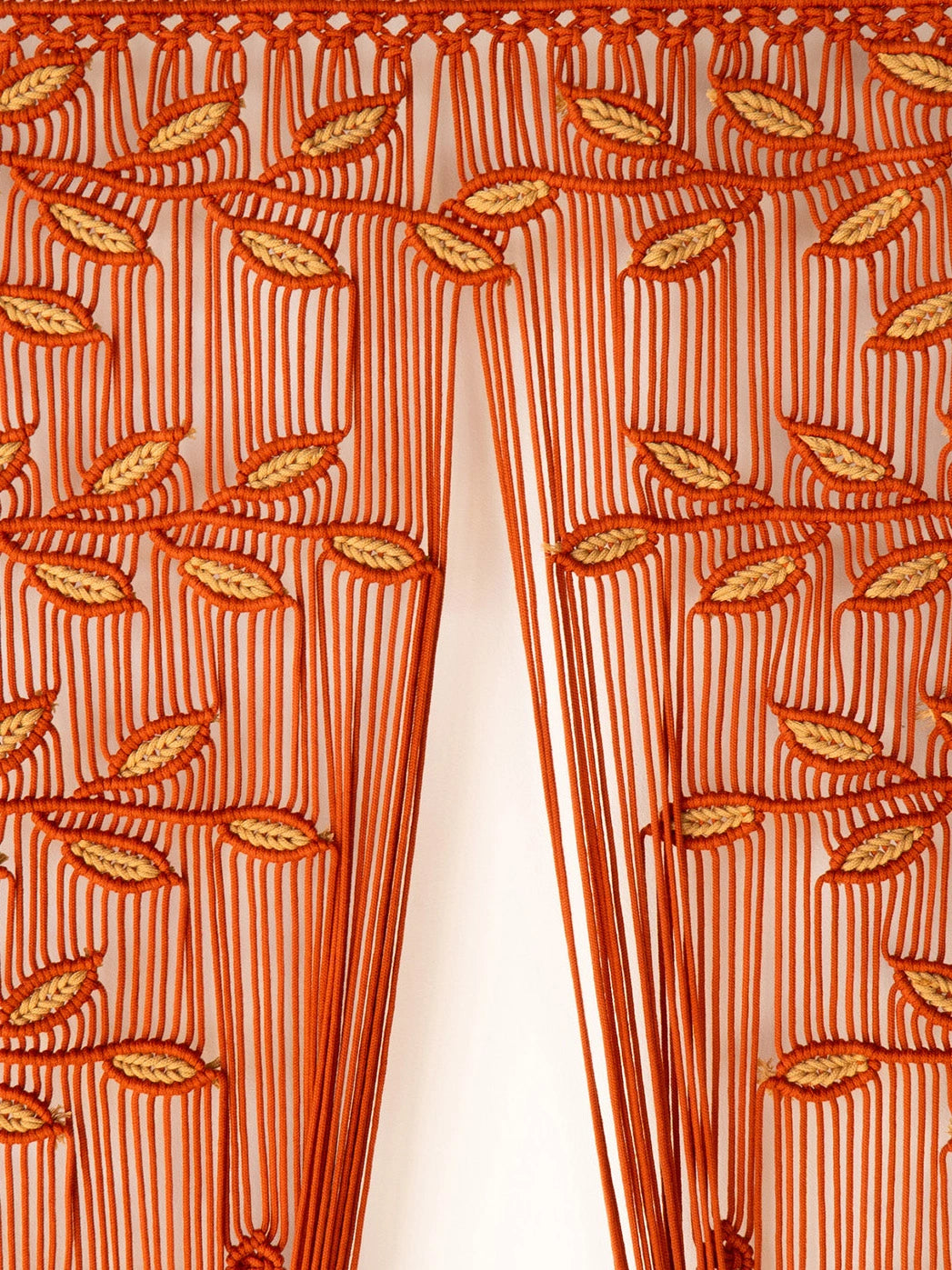 Close-up of an orange curtain panel with a leaf and stripe pattern, hanging in front of a white background.