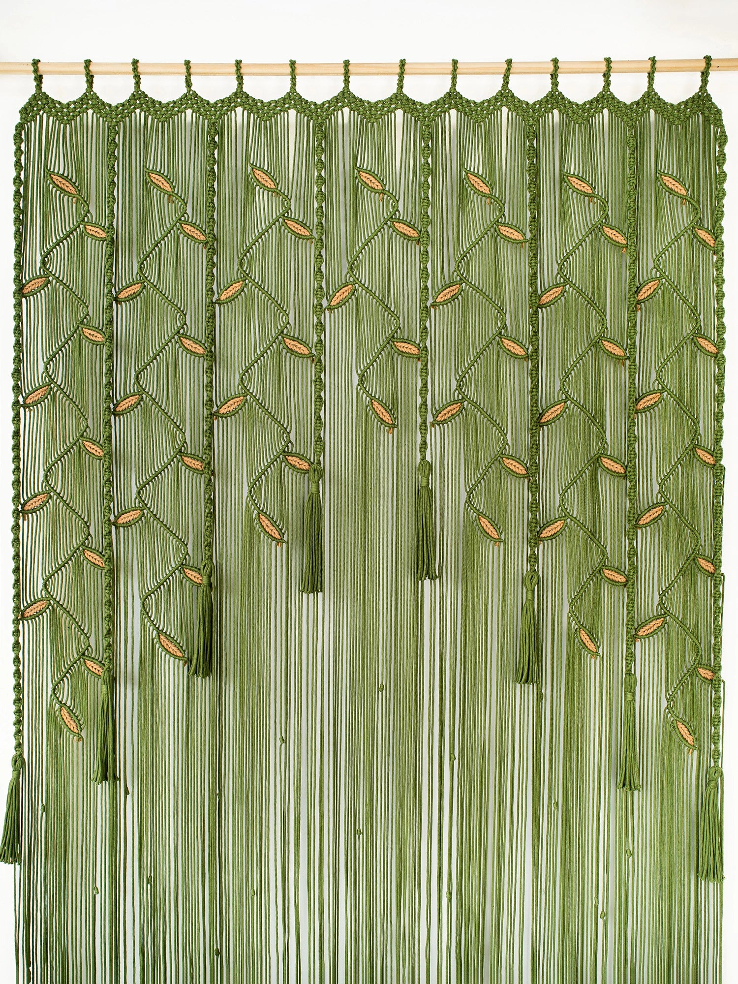 An olive green beaded curtain featuring vertical strands, leaf-like bead motifs, and hanging tassels, suspended from a light wood rod against a plain white wall.
