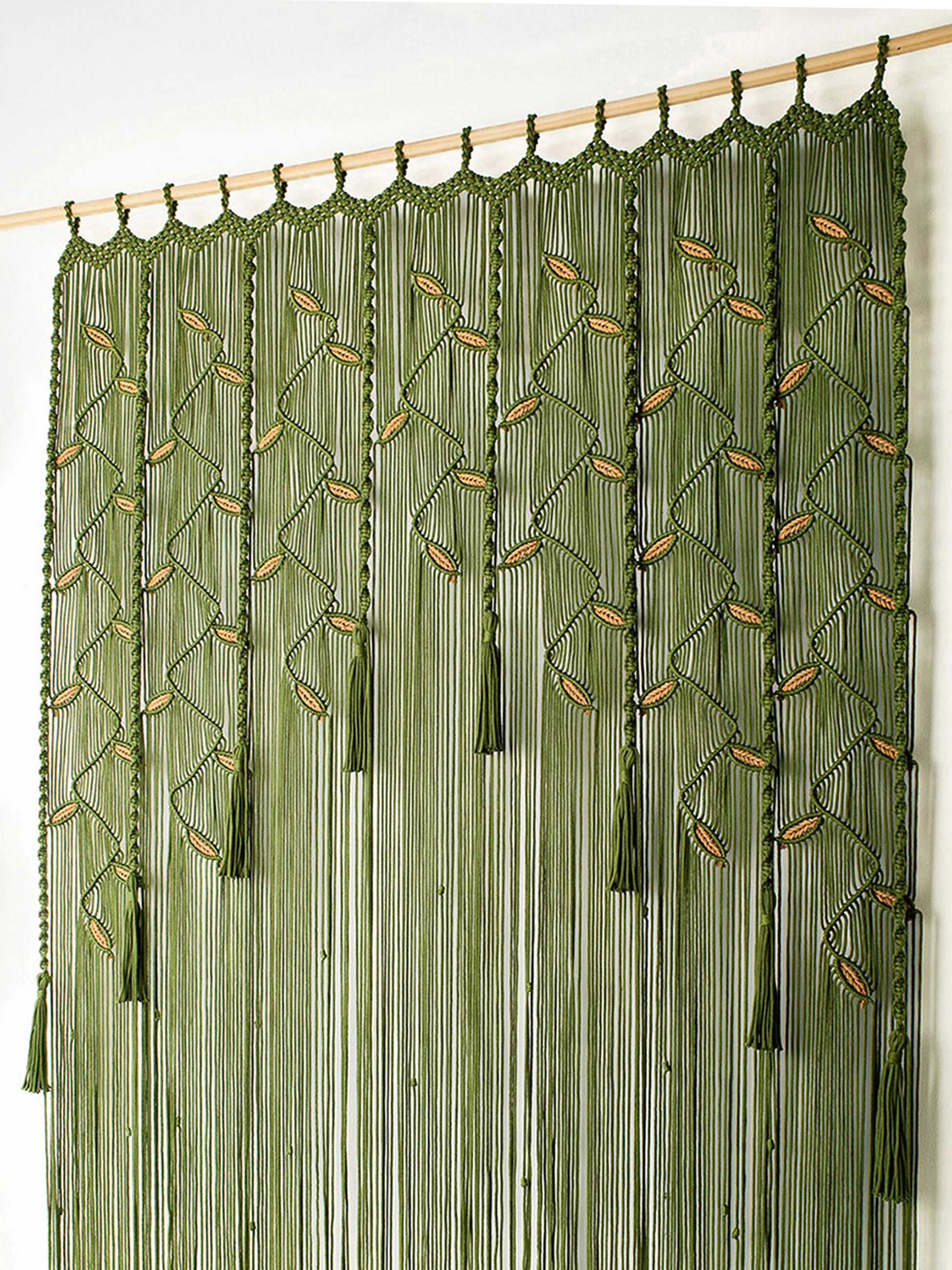 An olive green beaded curtain featuring vertical strands, leaf-like bead motifs, and hanging tassels, suspended from a light wood rod against a plain white wall.