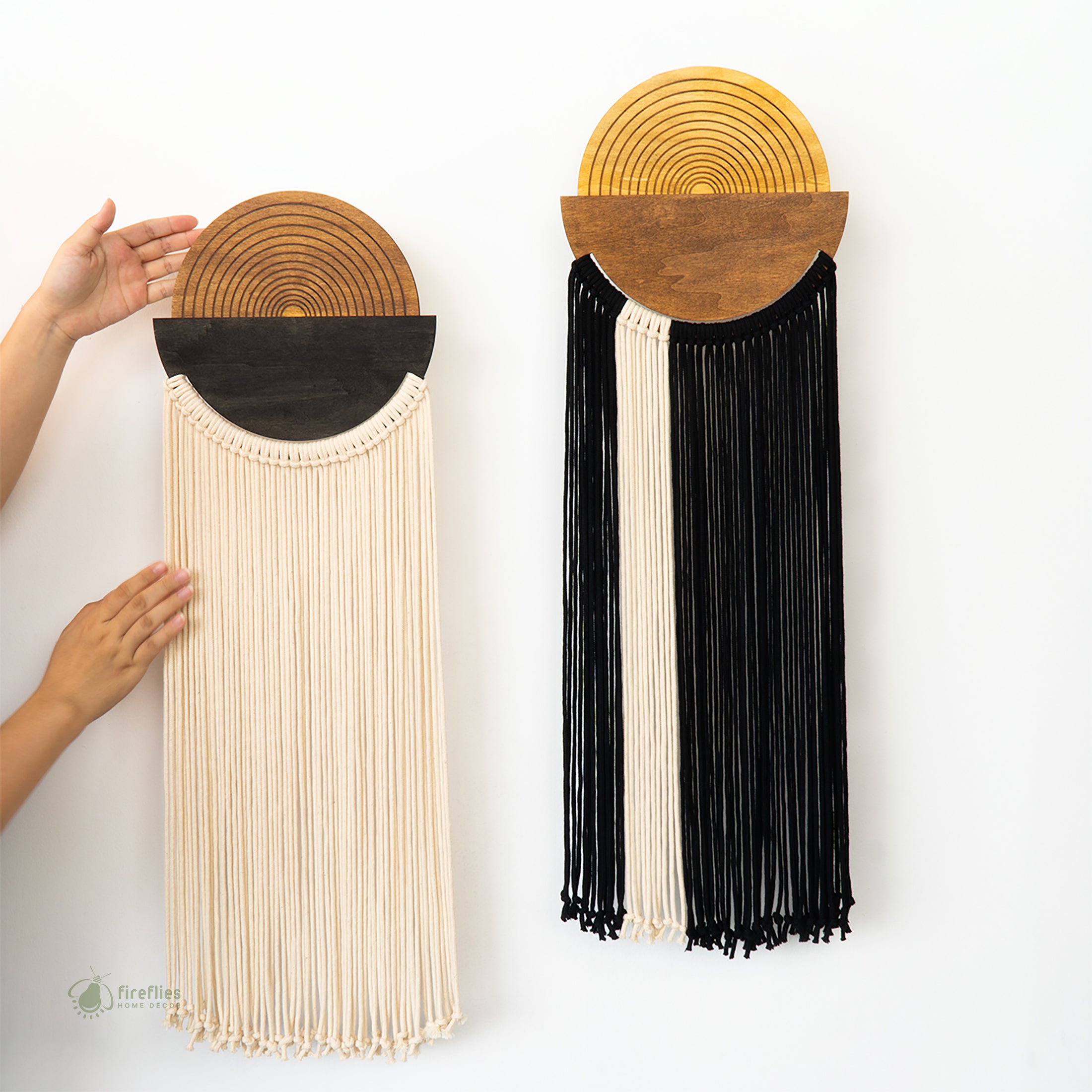Two wall hangings with circular wooden tops and long fringe made of yarn on a white background.