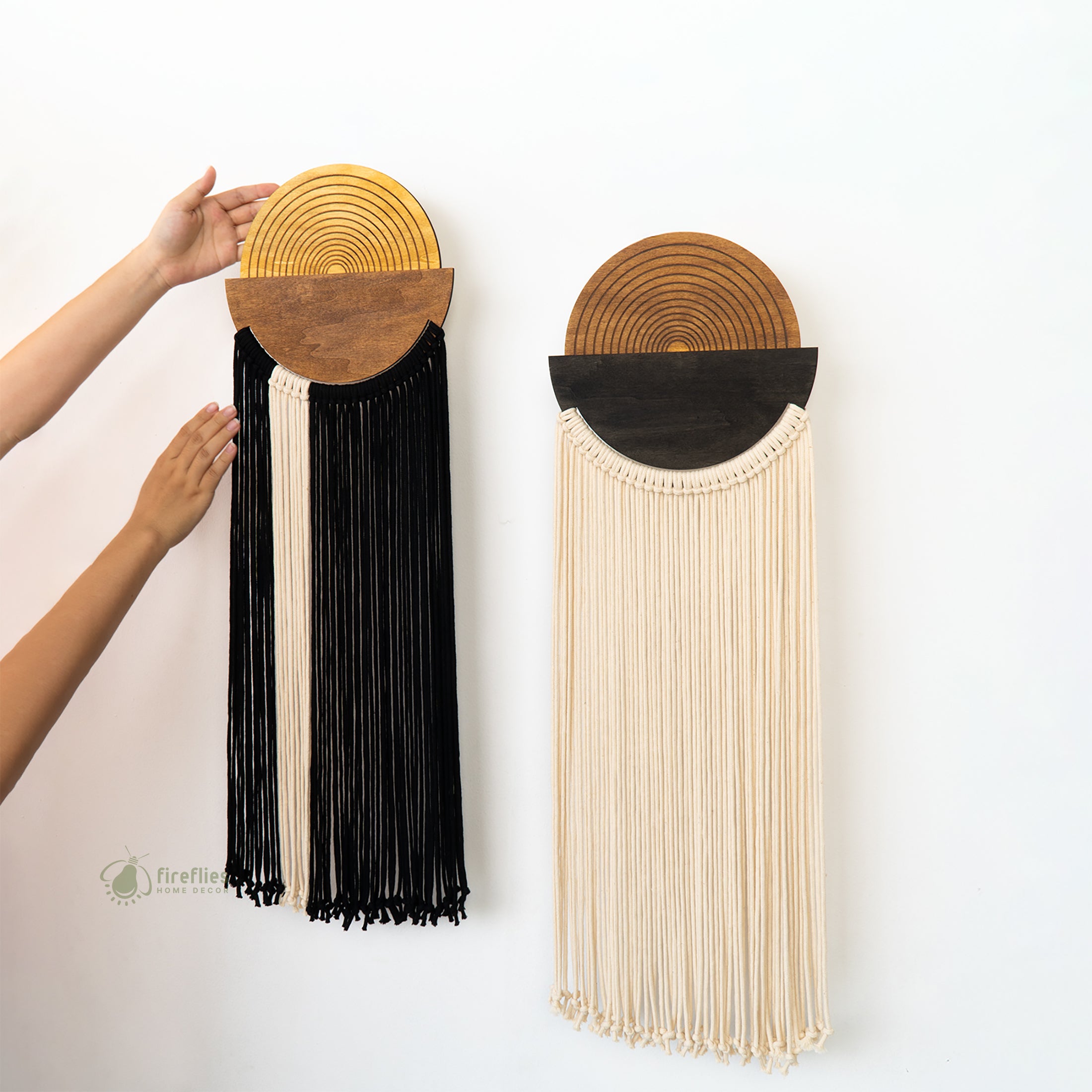 Two wall hangings with wooden top sections and long black and beige fringe on a white background.