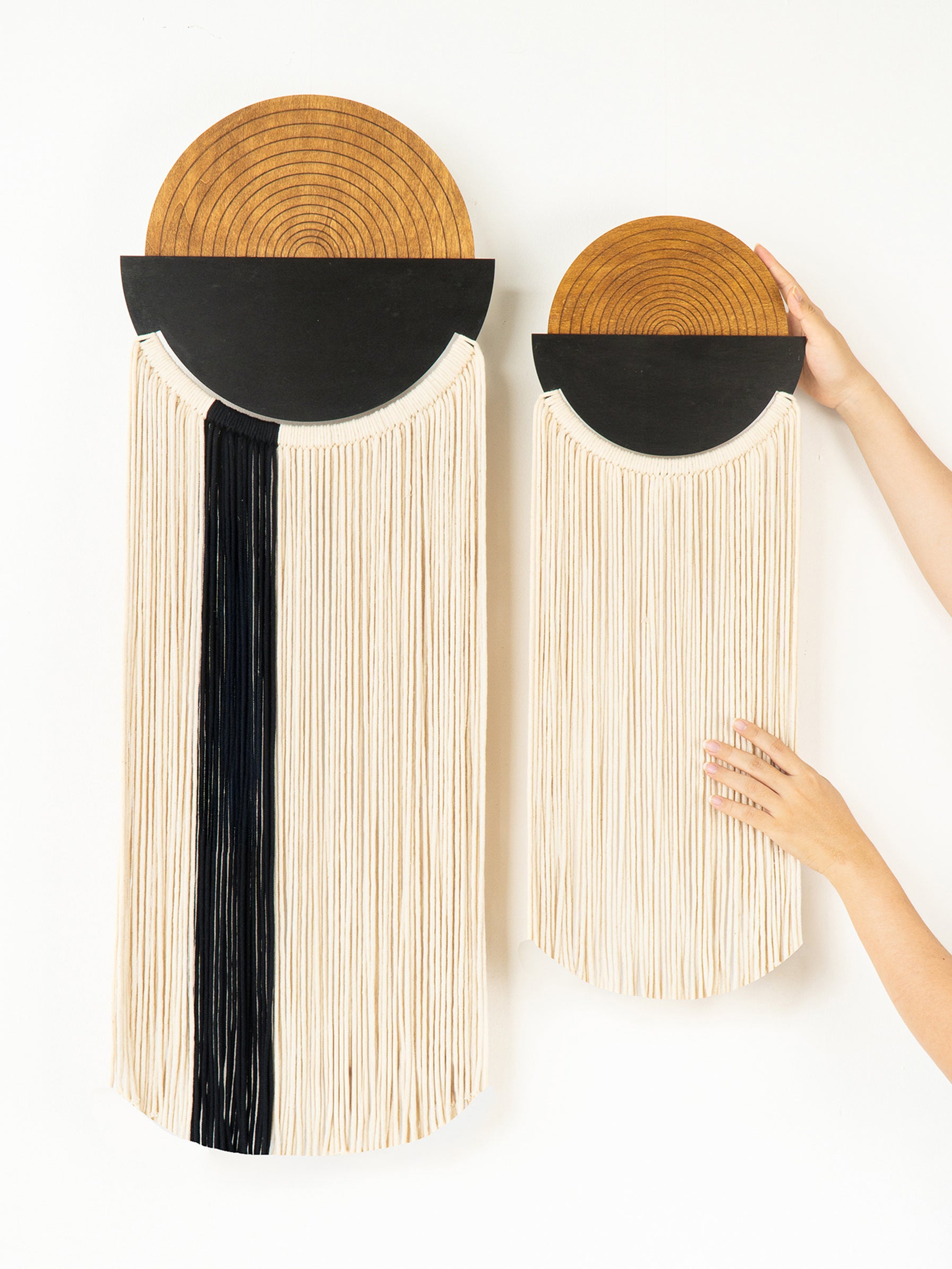 Two wall hangings with black and wooden circular designs on a white background