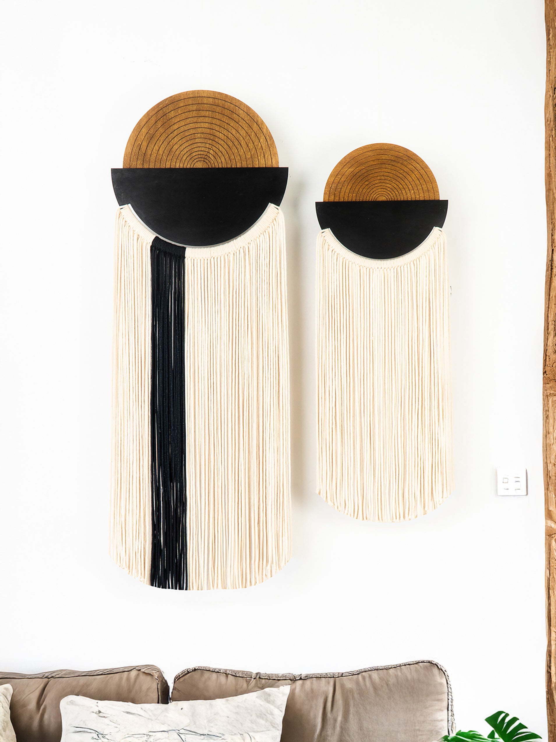 Two macrame Christmas tree wall hangings on a white wall with a cabinet and decorative items in the background.