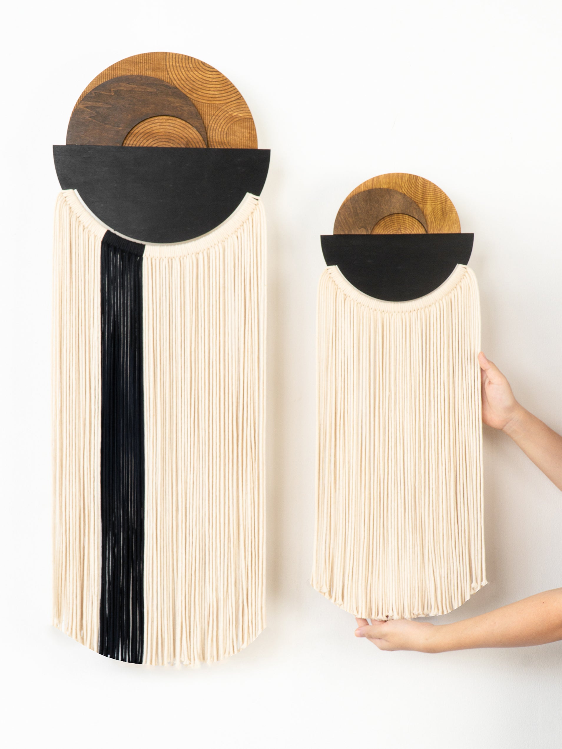 Two wall-mounted woven baskets with black accents, one being held by a hand.