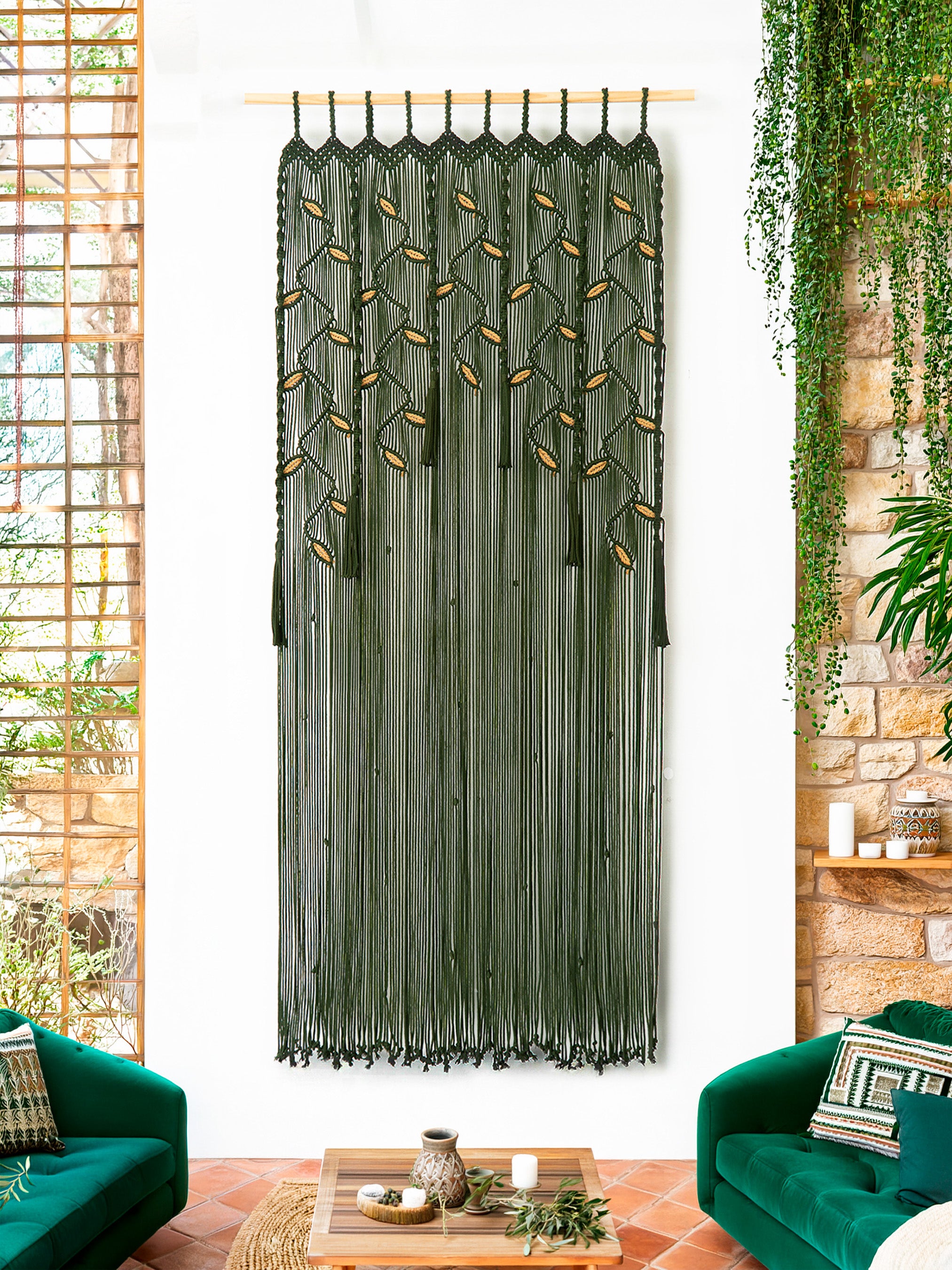 Decorative green macrame curtain hanging in a living room with green sofas and a wooden coffee table.