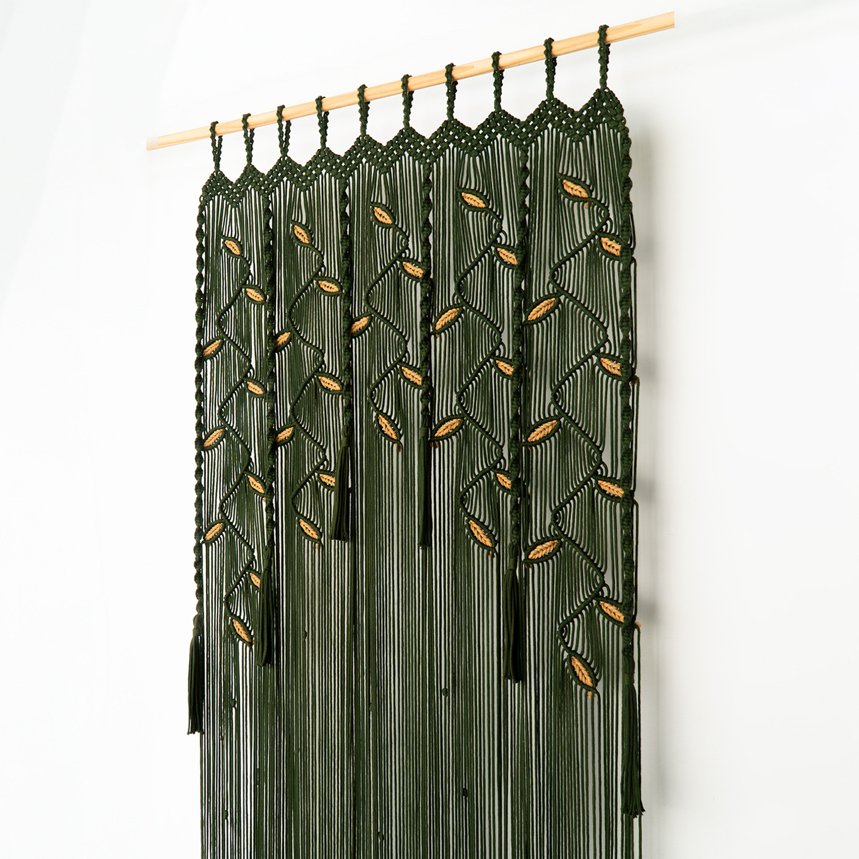Macrame curtain with leaf patterns on a wooden rod against a white background