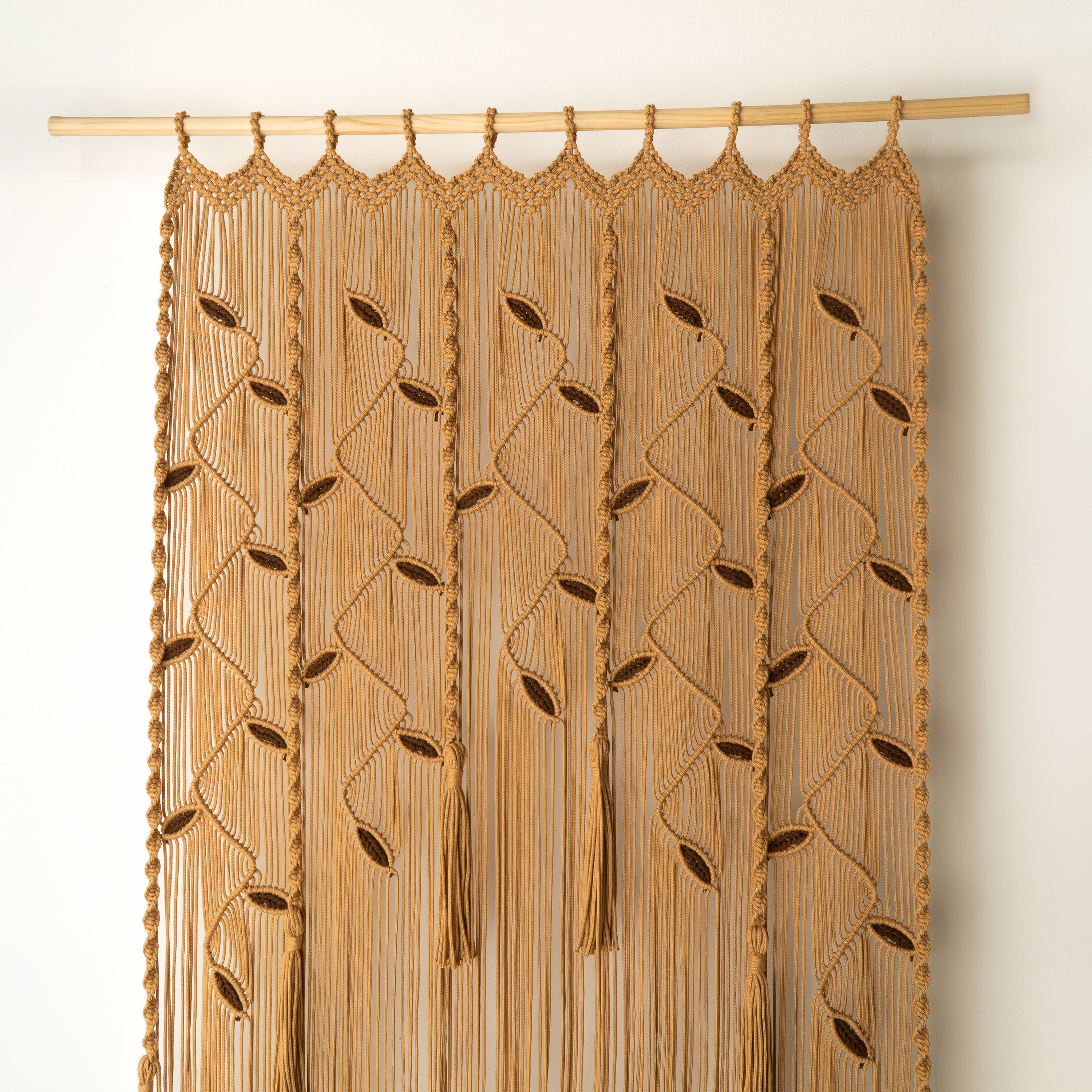 Macrame curtain with leaf patterns on a wooden rod against a beige wall