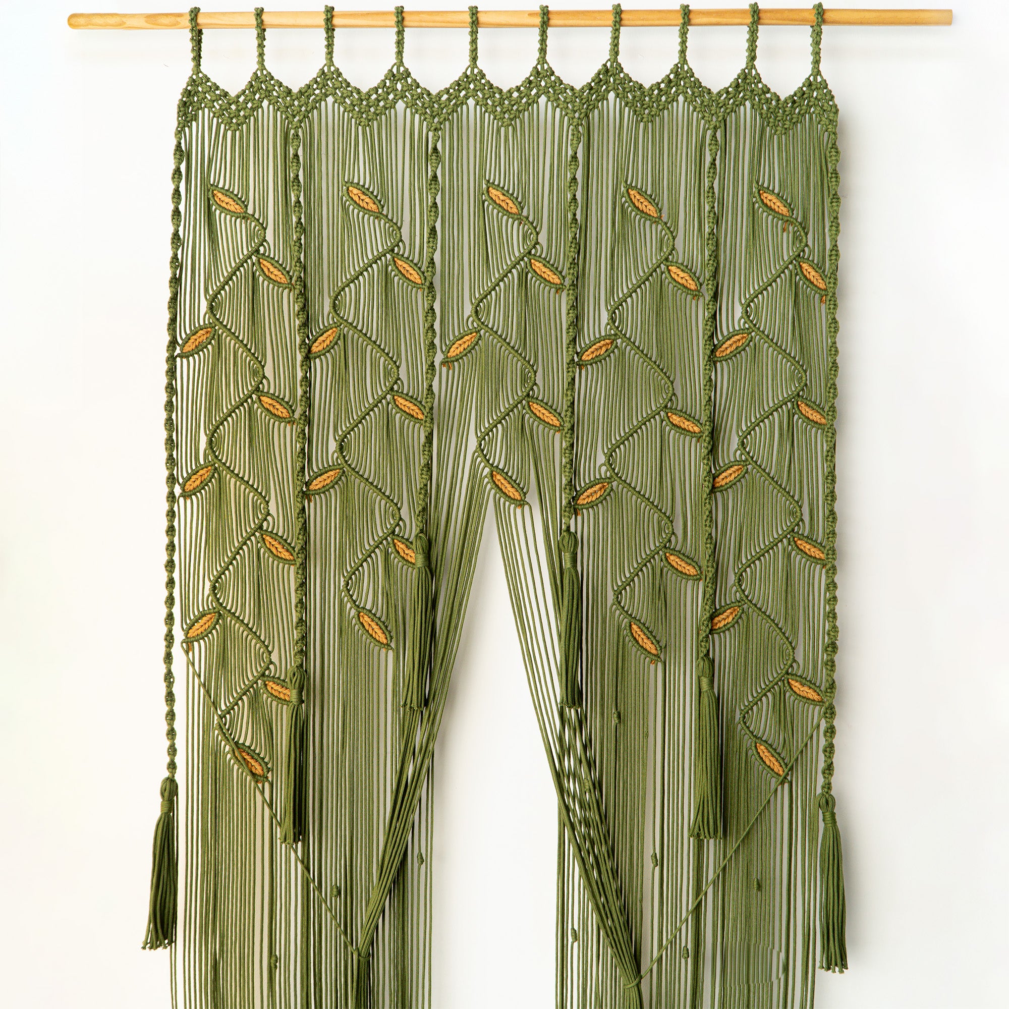 Green macrame curtain with tassels on a white background