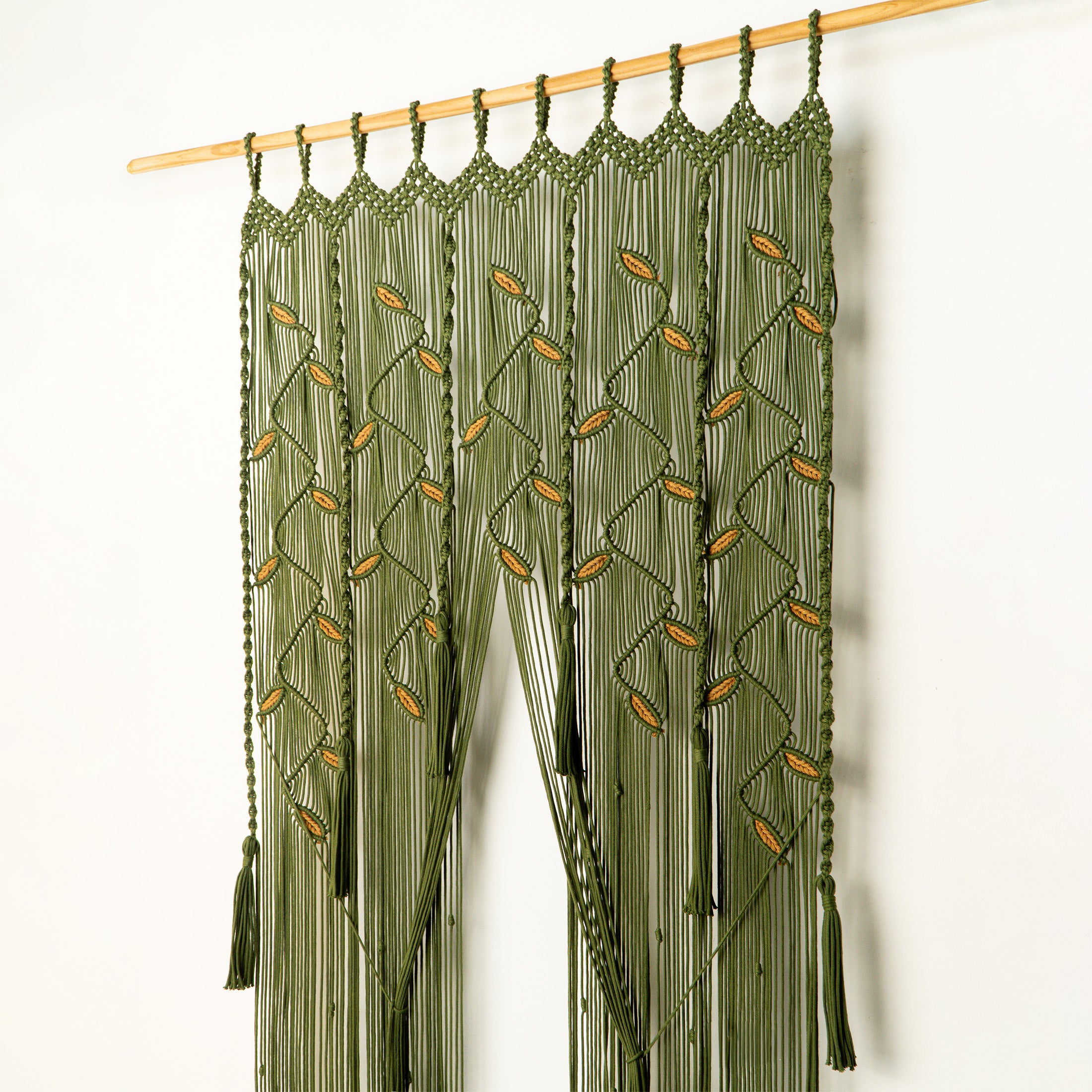Green macrame curtain with tassels hanging on a wooden rod against a white background