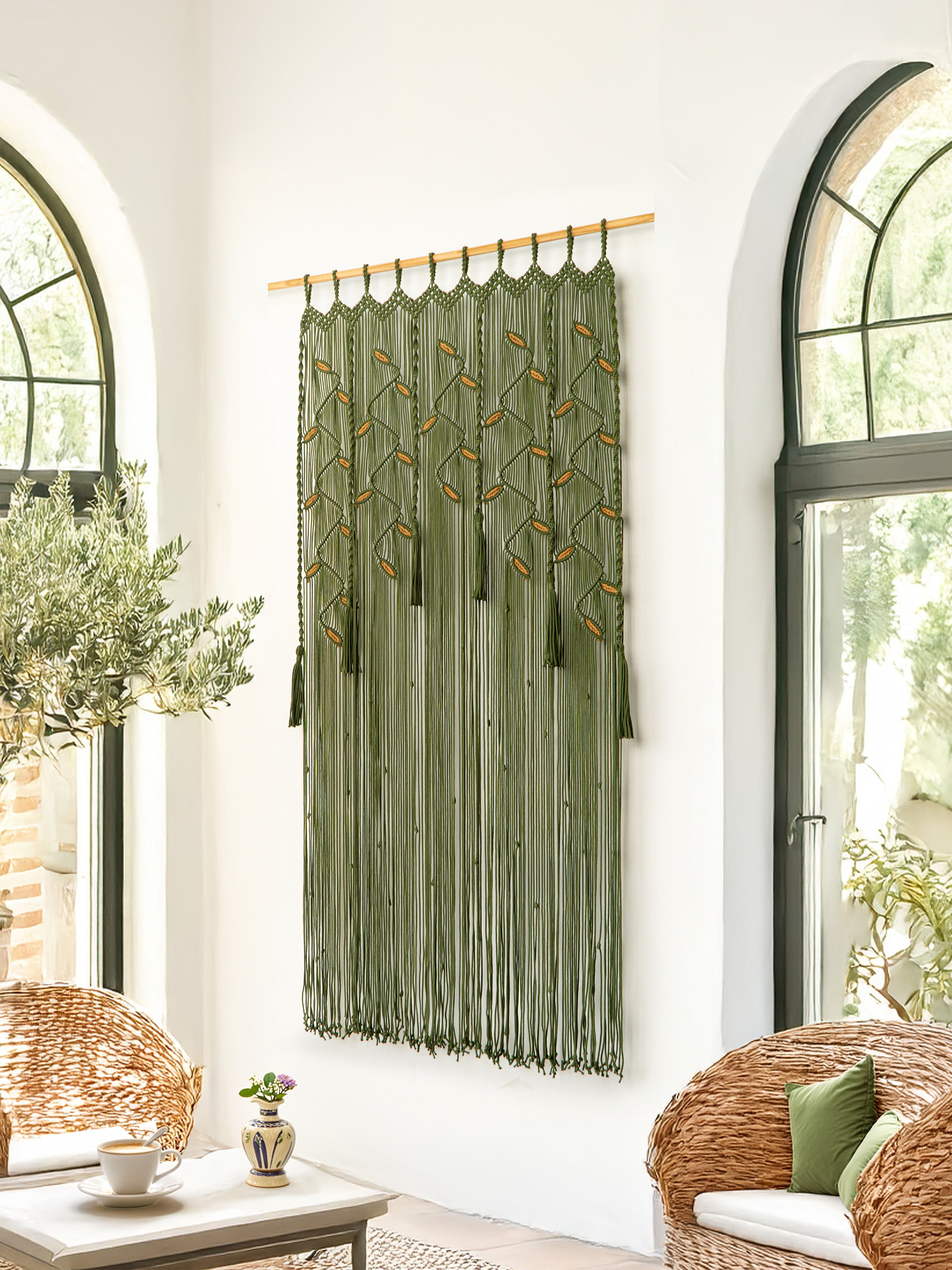 Decorative green curtain with tassels hanging in a room with wicker furniture and large windows.