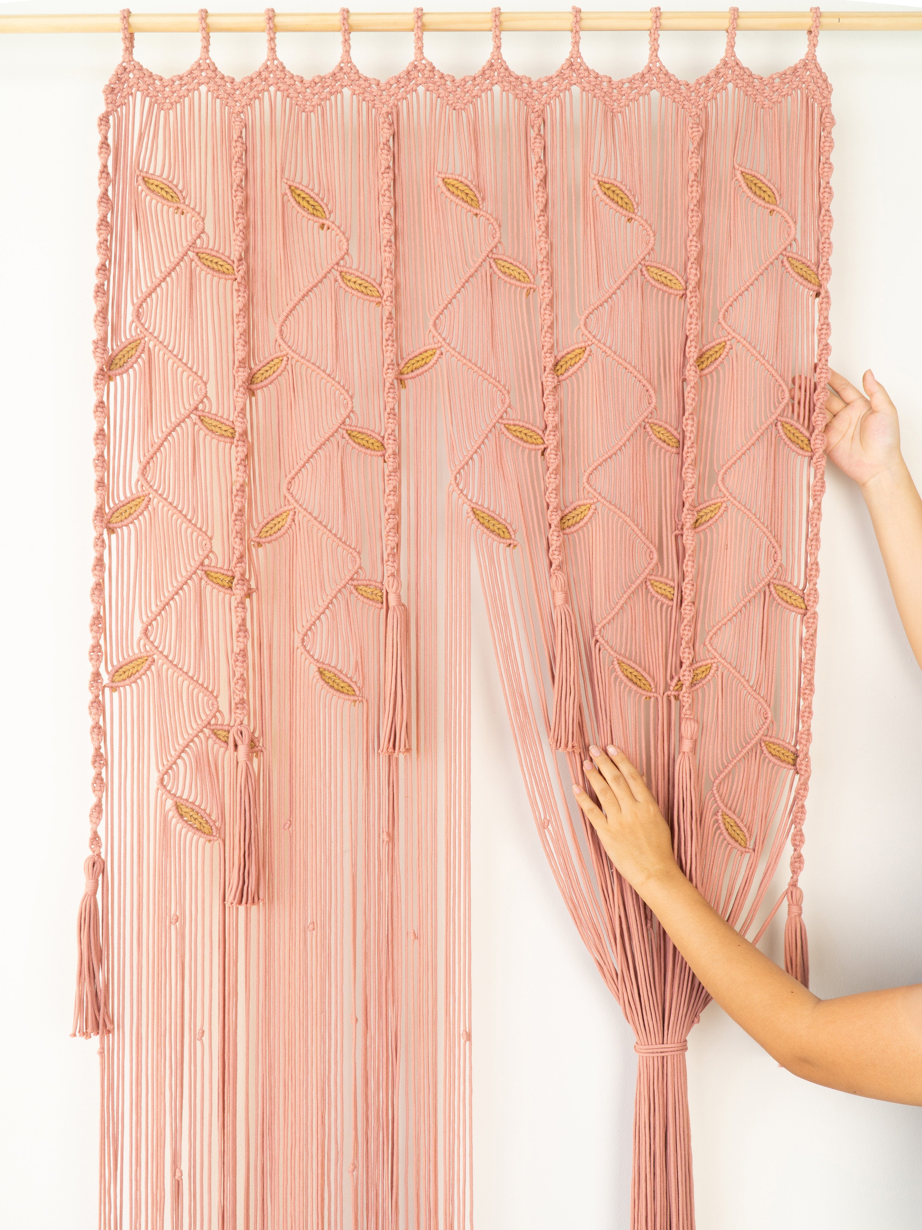 Pink macrame curtain with geometric patterns on a white background