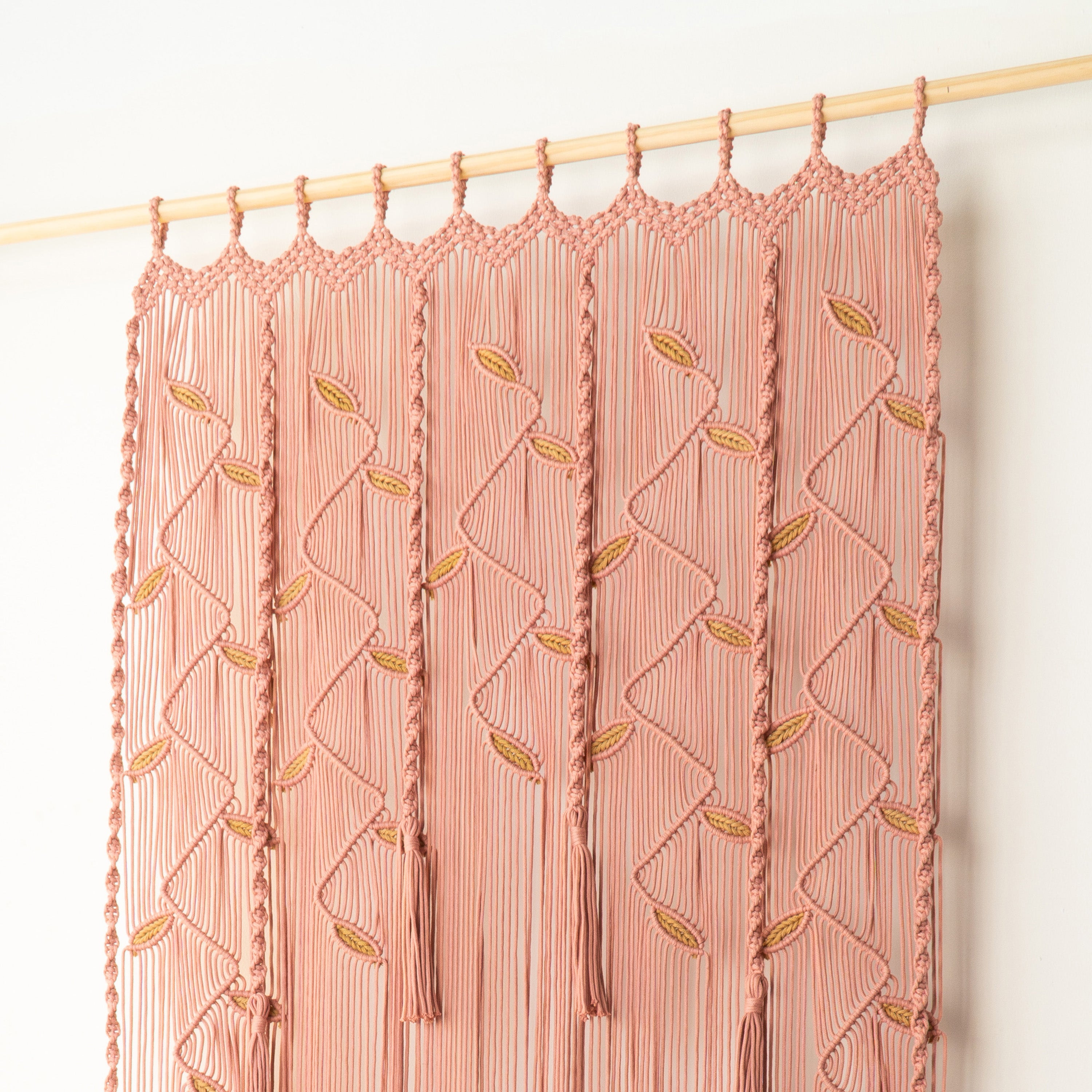 Pink macrame wall hanging with geometric pattern on a wooden rod against a white background