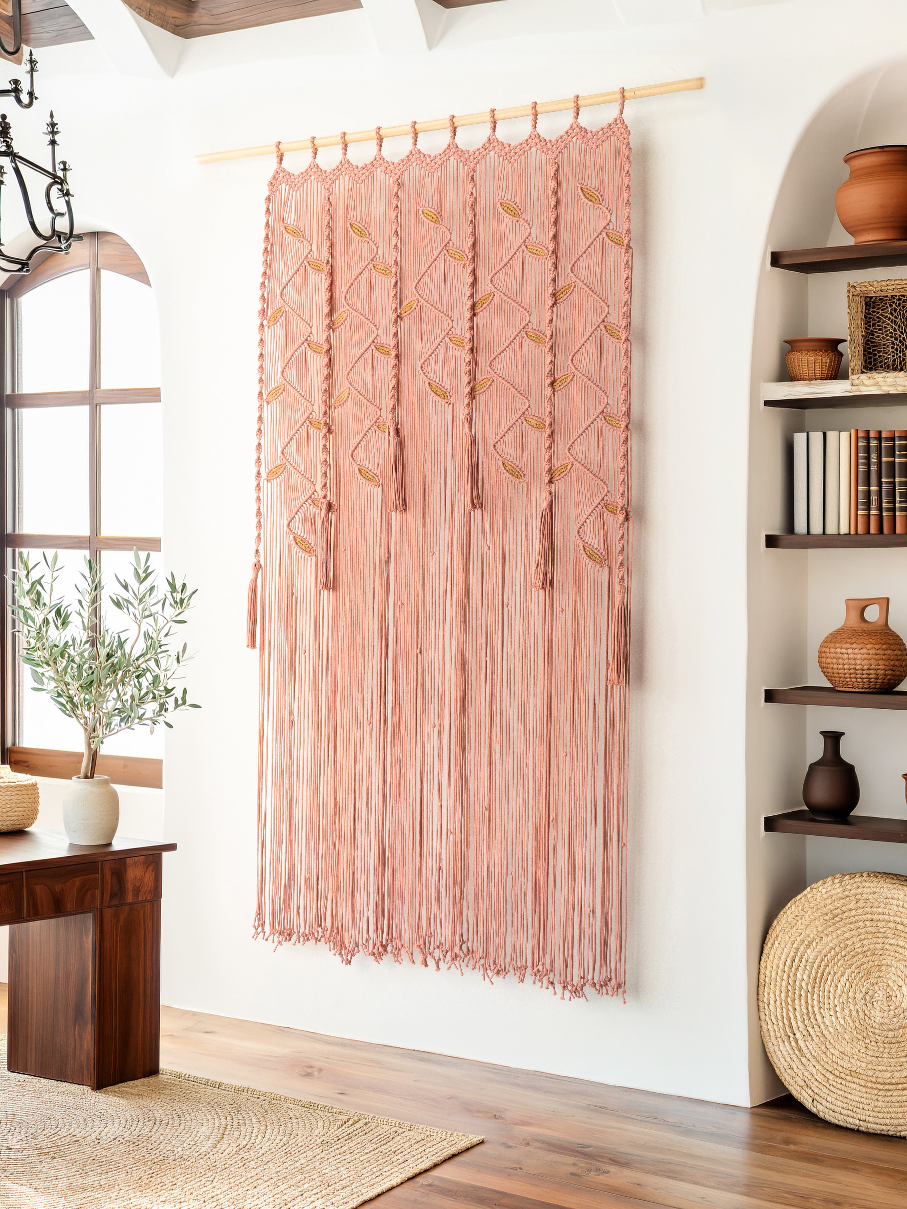Pink macramé wall hanging in a room with wooden floor, window, and shelves.