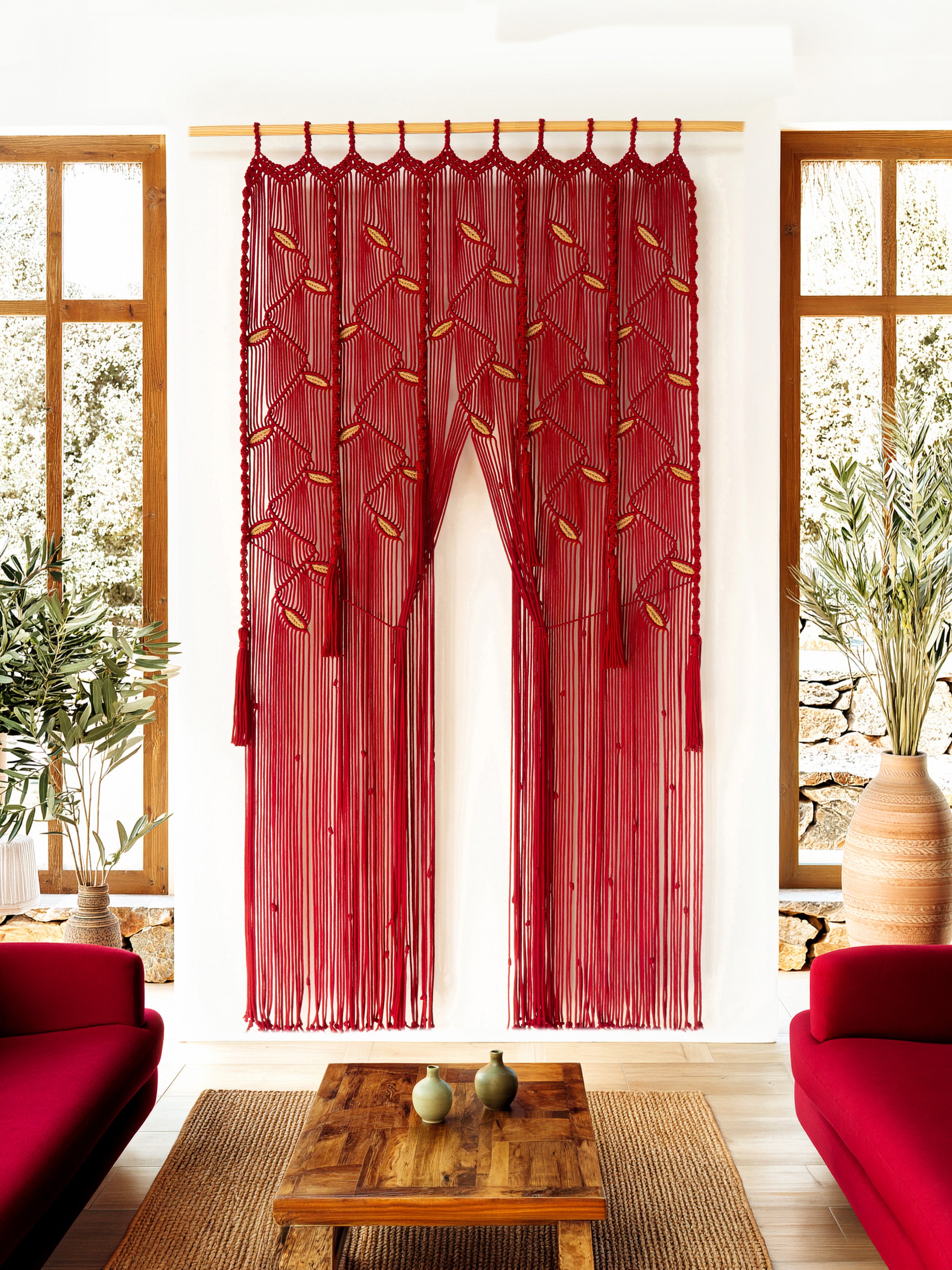Red embroidered curtain hanging between two windows in a room with red furniture and a wooden table.