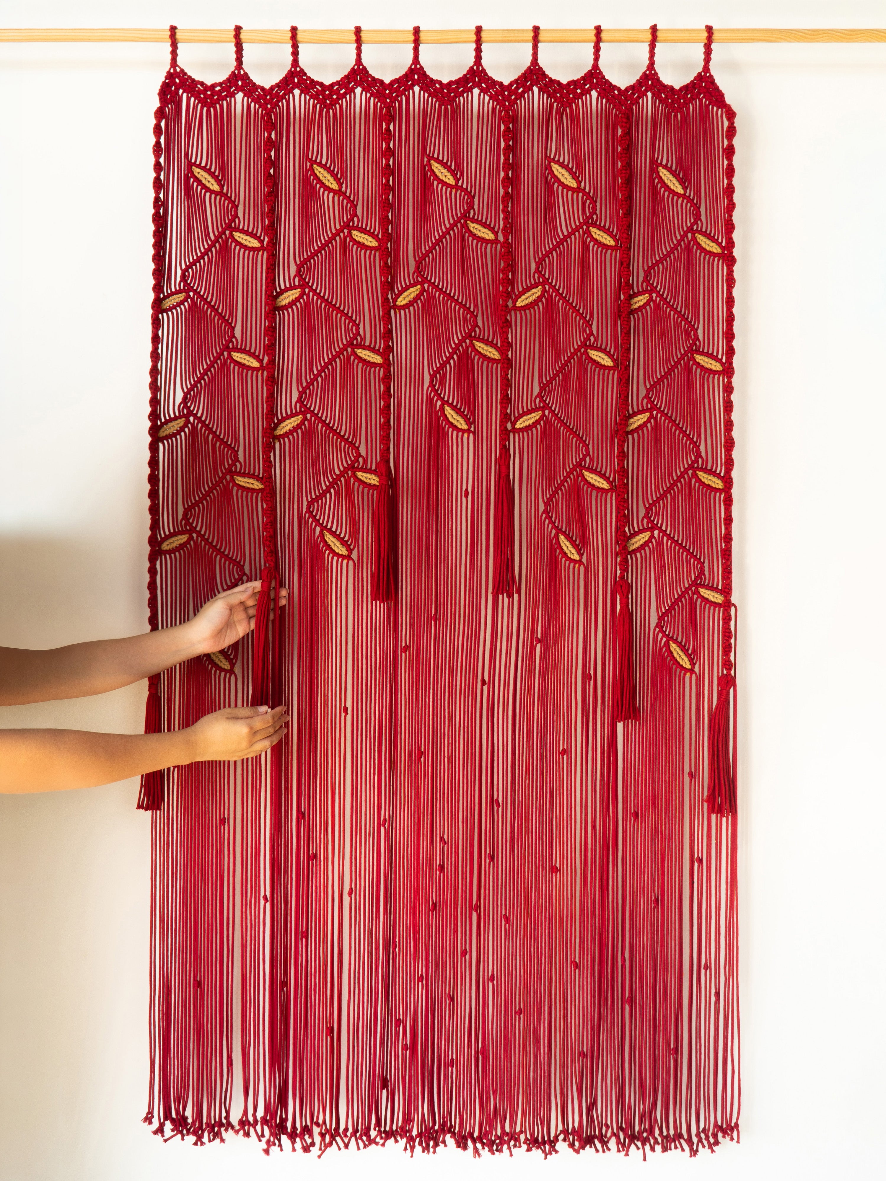 Red string curtain with intricate patterns on a wooden rod against a white wall.
