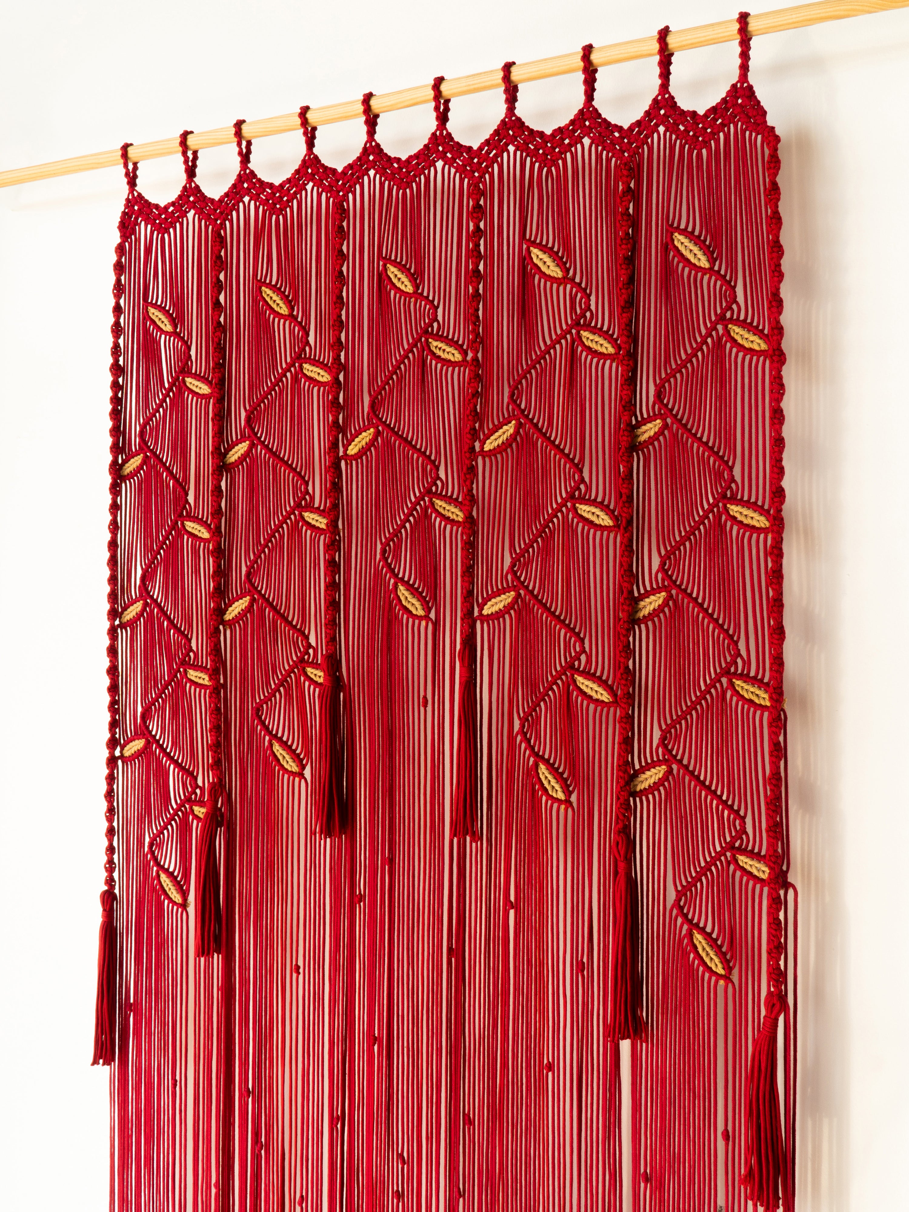 Red macrame curtain with gold accents on a white background