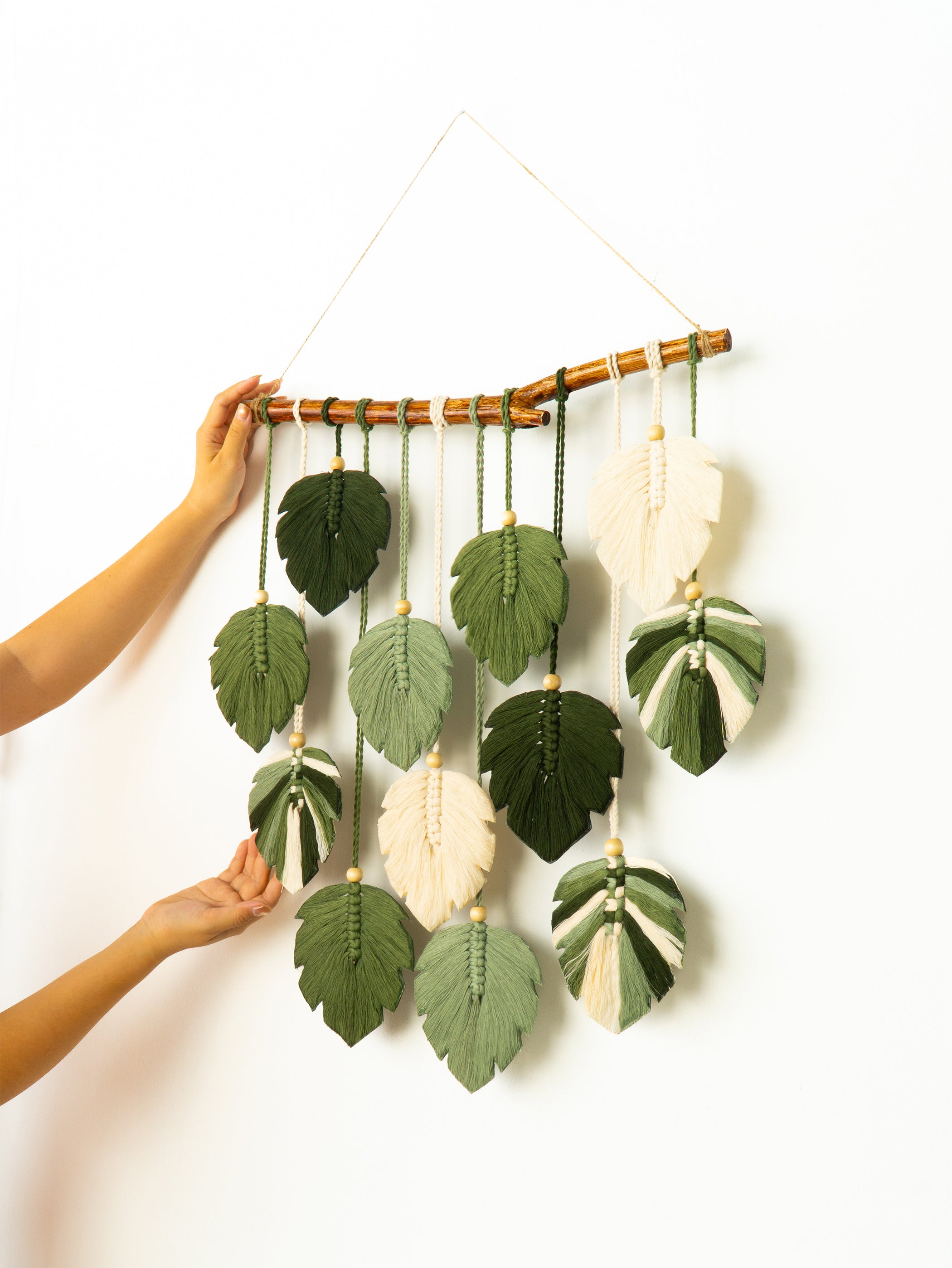 Handmade wall hanging with leaf-shaped decorations on a white background