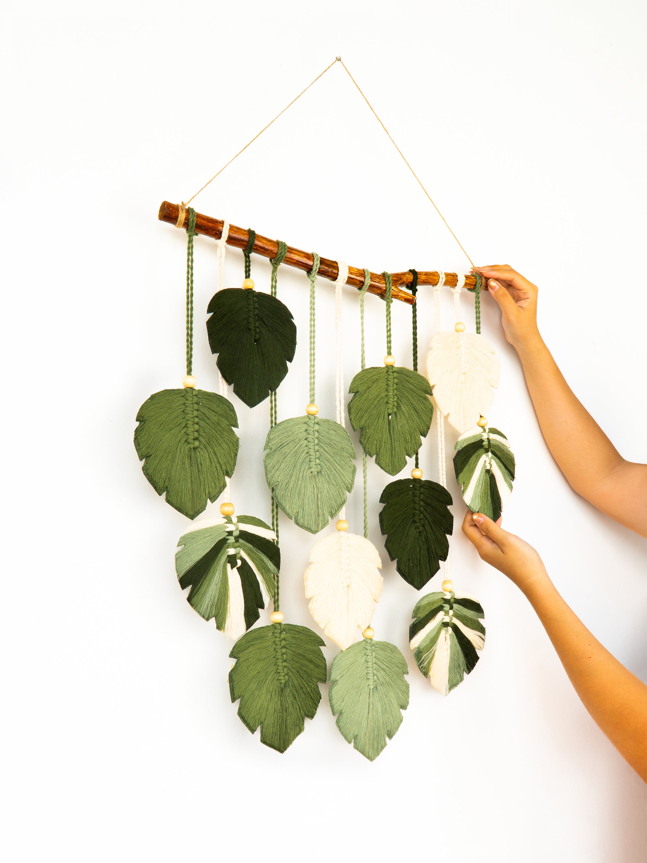 Decorative wall hanging with green leaves and white balls on a white background
