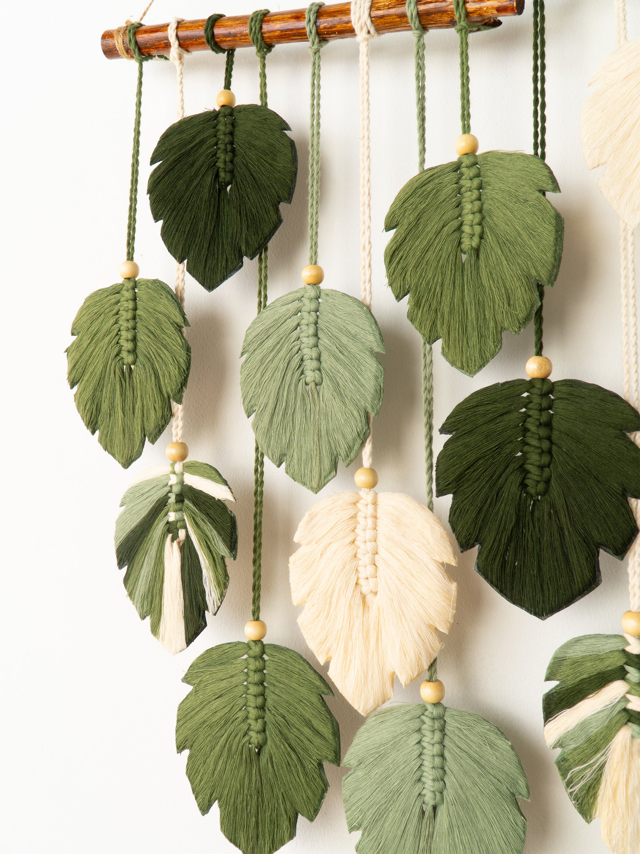 Decorative wall hanging with green leaf-shaped tassels and a central cream-colored feather on a white background.