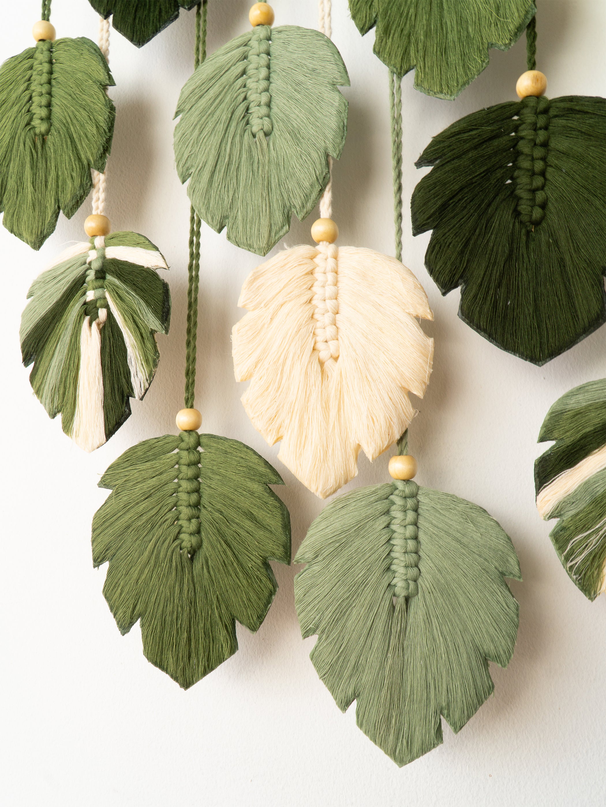 Macrame leaf decorations in green, white, and brown on a white background