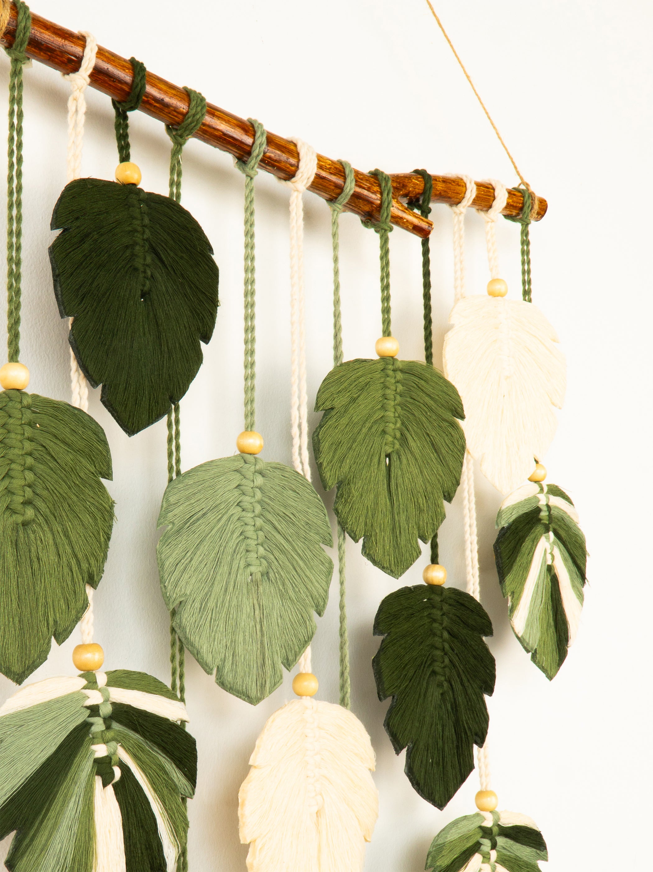 Decorative wall hanging with green and beige leaf-shaped yarn elements on a neutral background