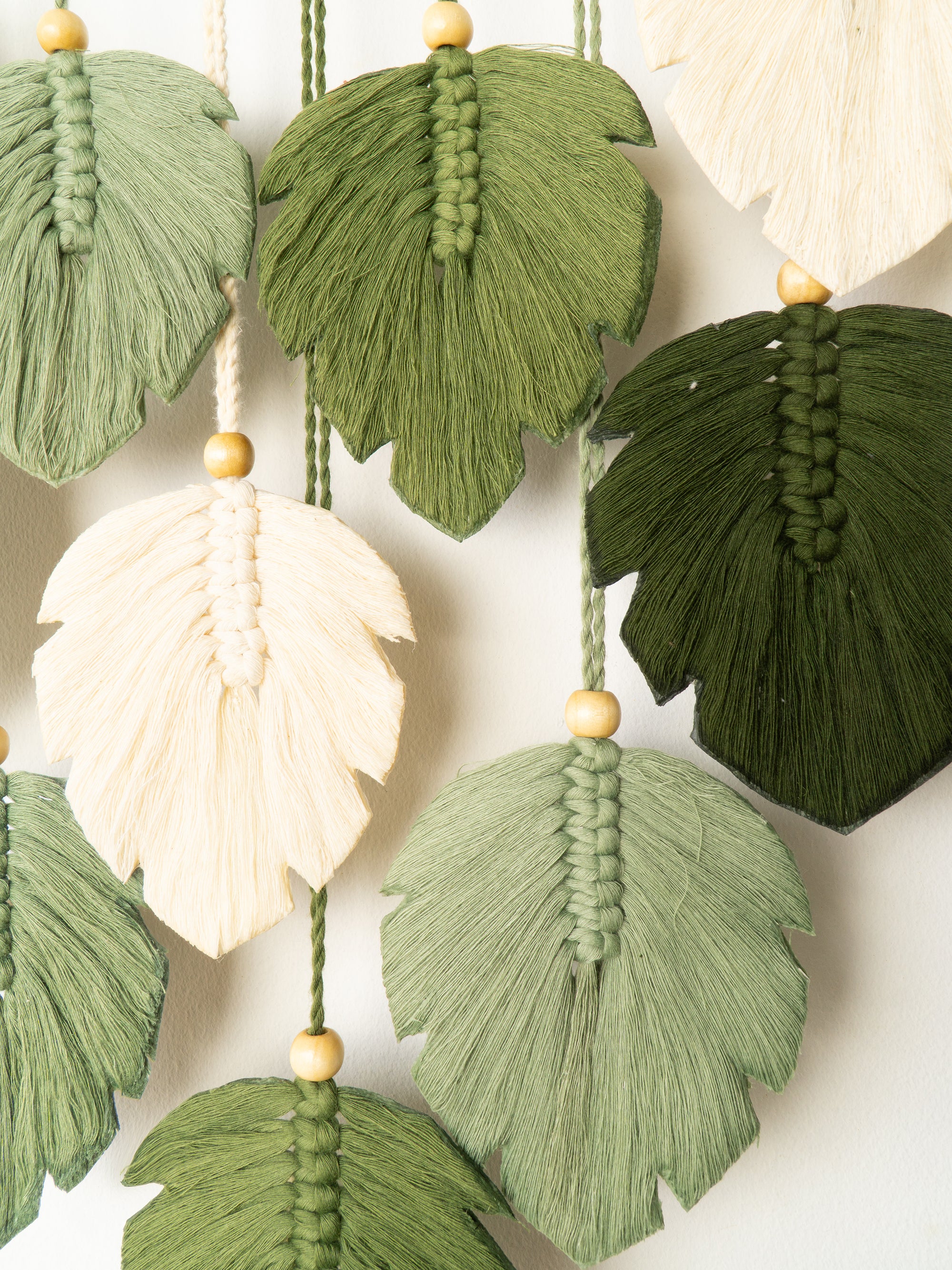 Macrame leaf decorations in green, white, and brown on a neutral background