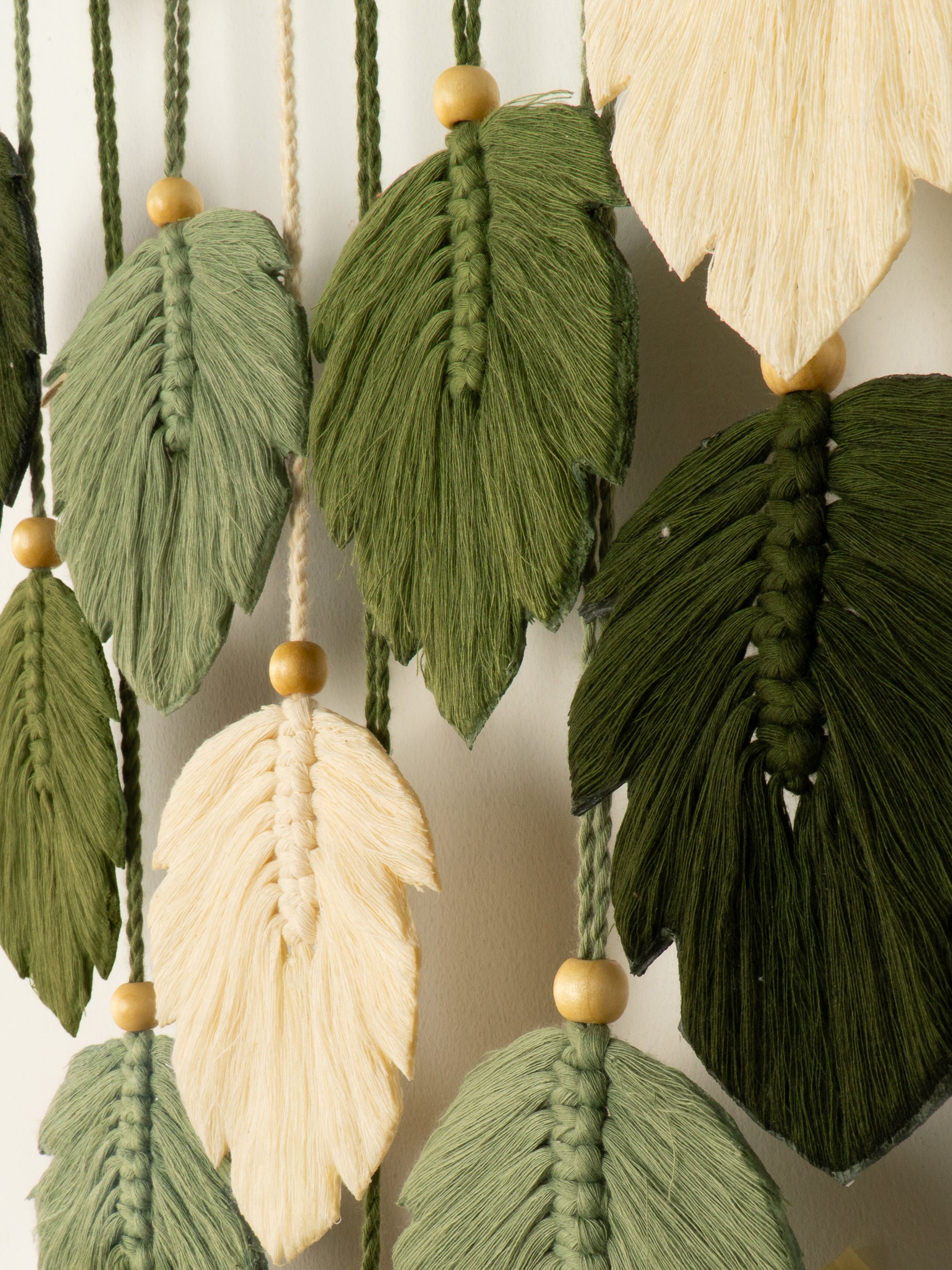 Decorative wall hanging with green and beige leaf-shaped yarn pieces on a neutral background