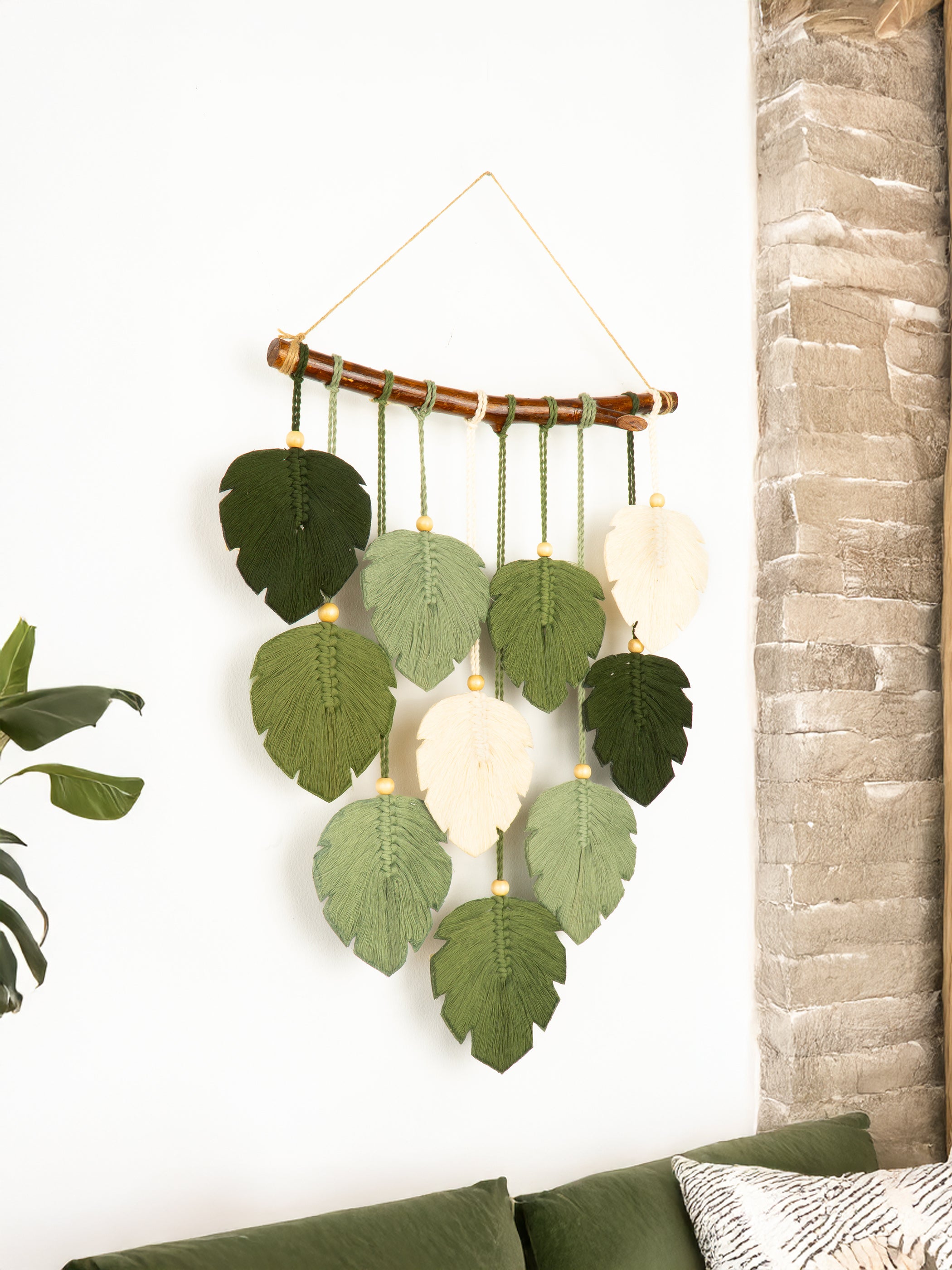 Decorative wall hanging with green leaves and white spheres against a white wall.