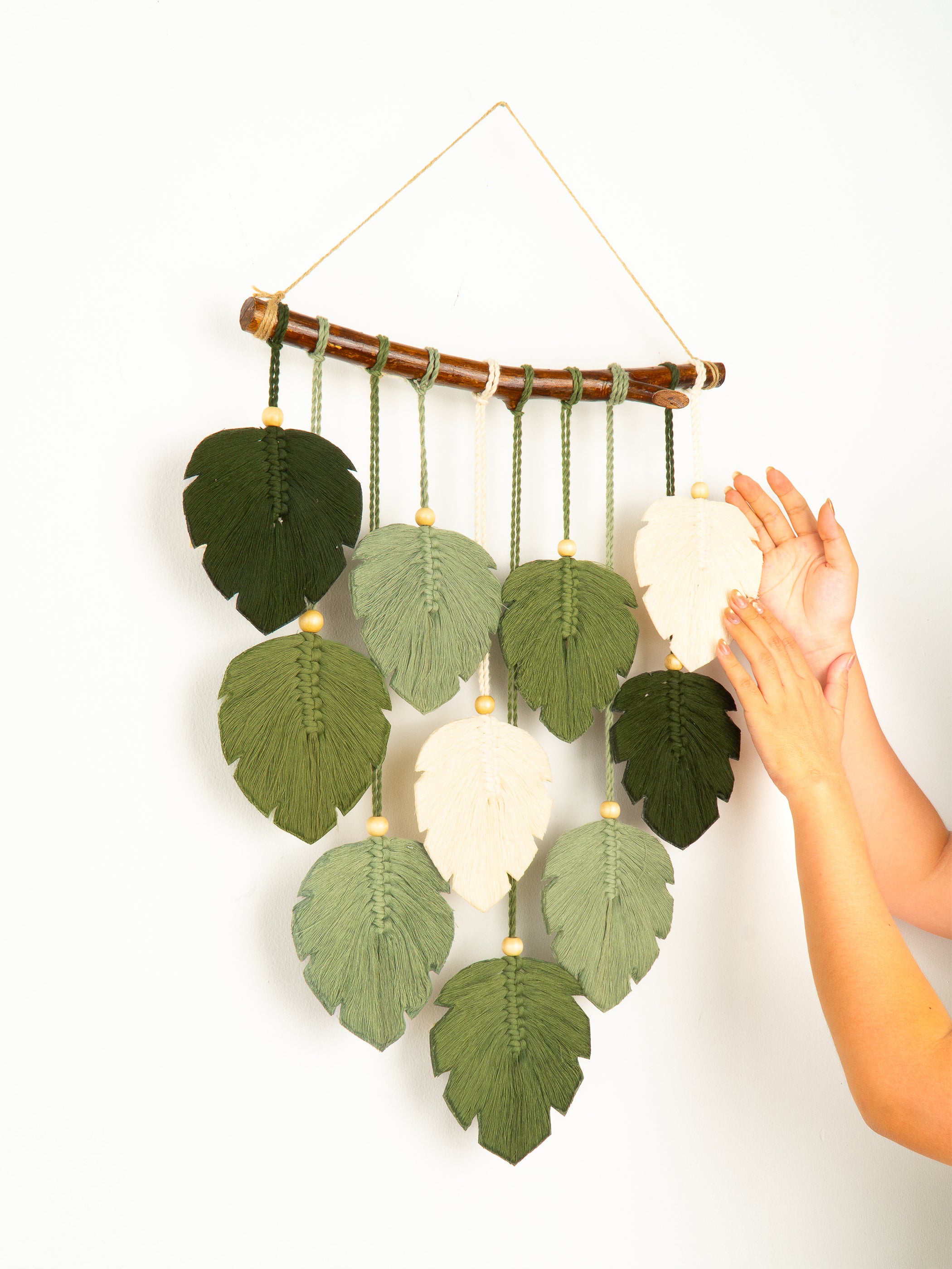 Decorative wall hanging with leaf-shaped leaves and a hand touching it on a white background