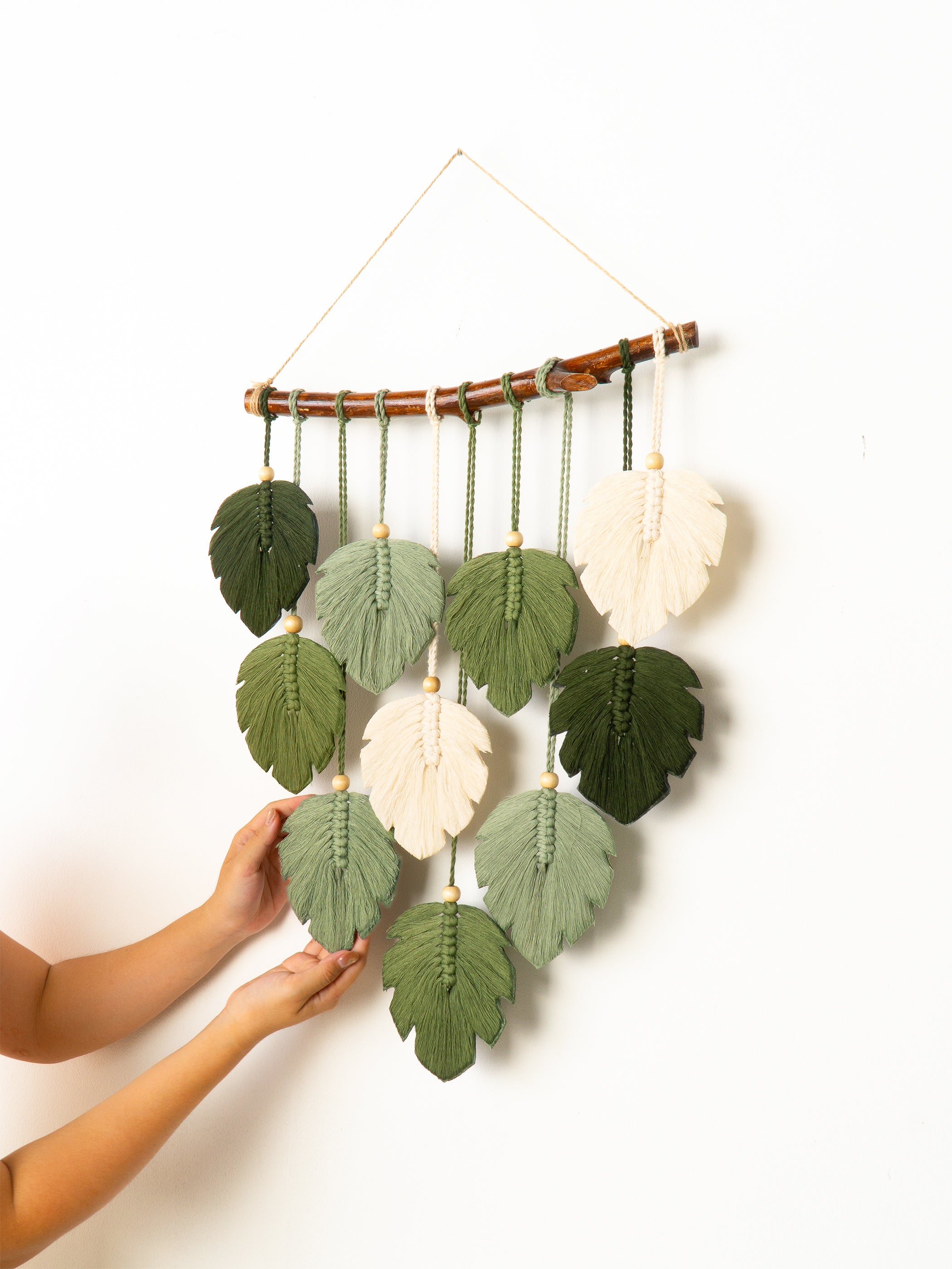 Handmade wall hanging with leaf-shaped decorations on a white background