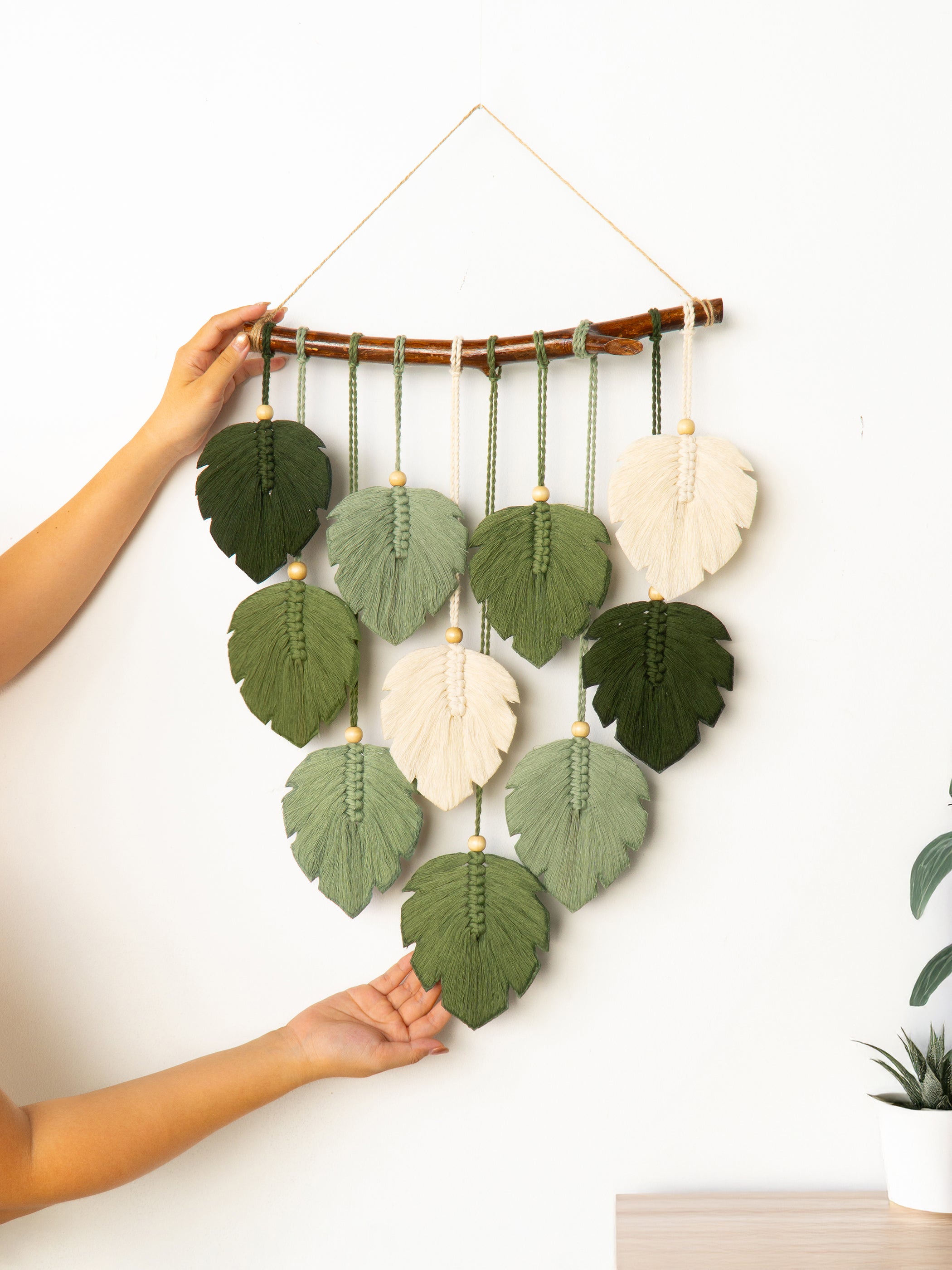 Handmade leaf wall hanging with green and white leaves on a white wall.