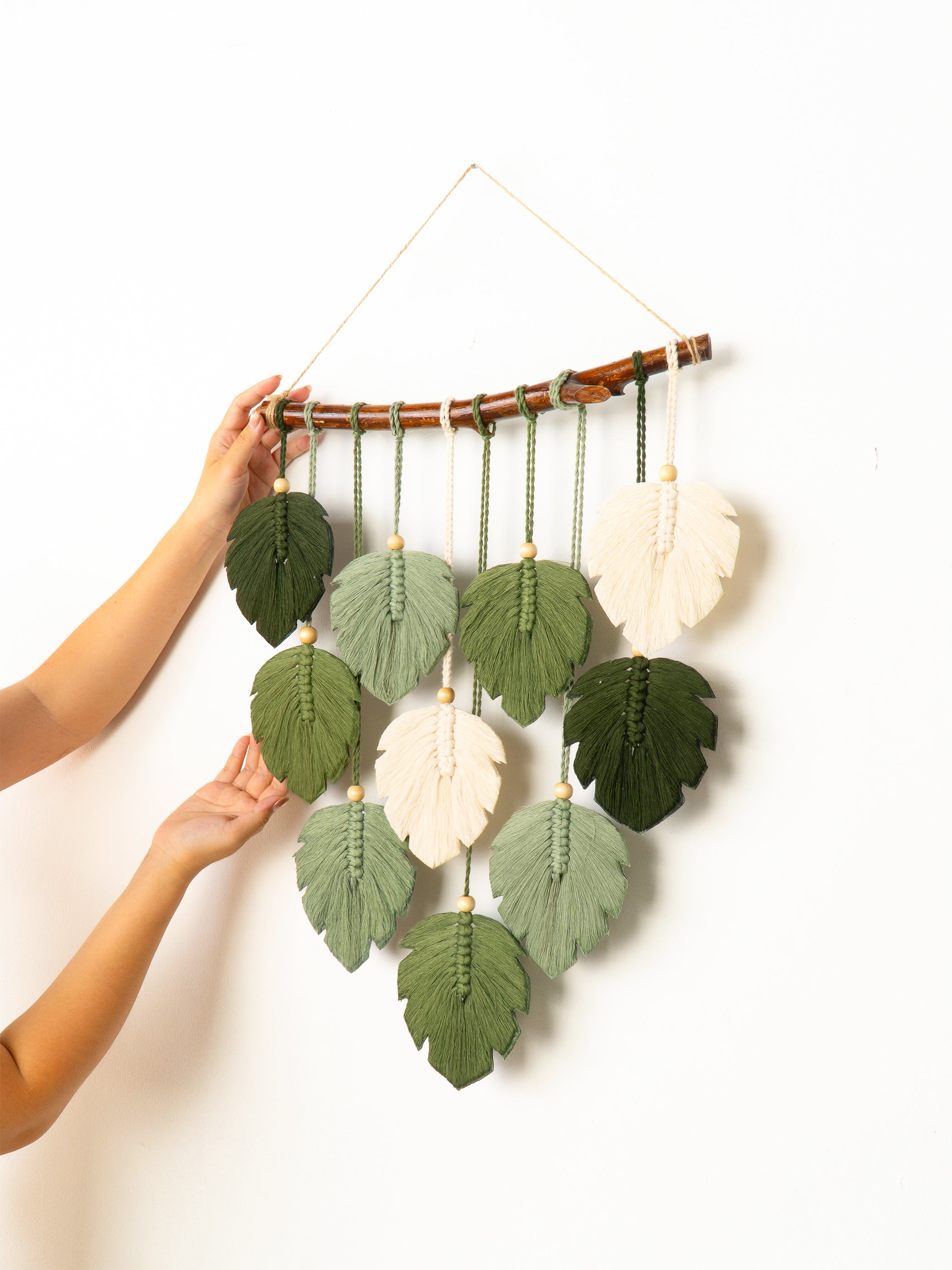Wall hanging with leaf-shaped decorations held by a person against a white background