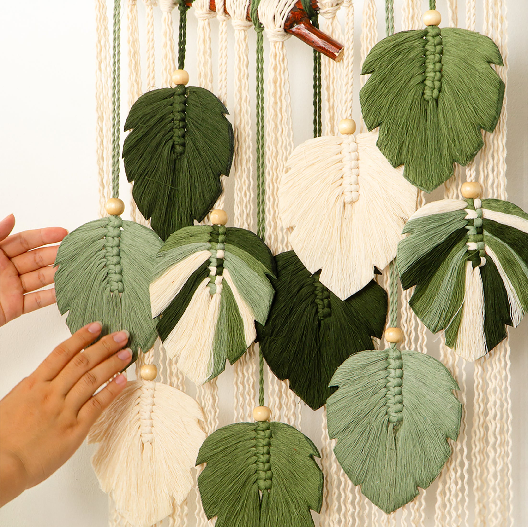 Macrame wall hanging with leaf-shaped decorations and a hand touching it.