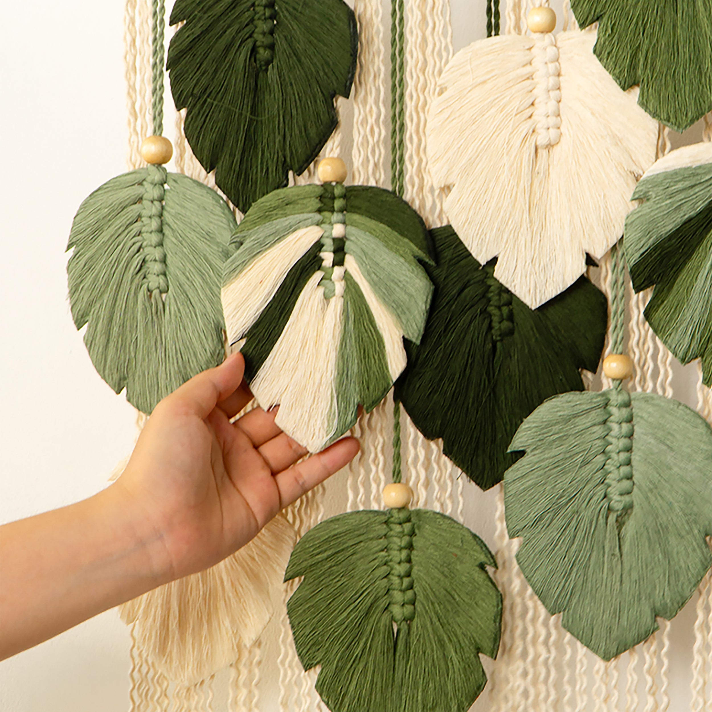 Hand holding a green tassel leaf against a wall with more tassels.