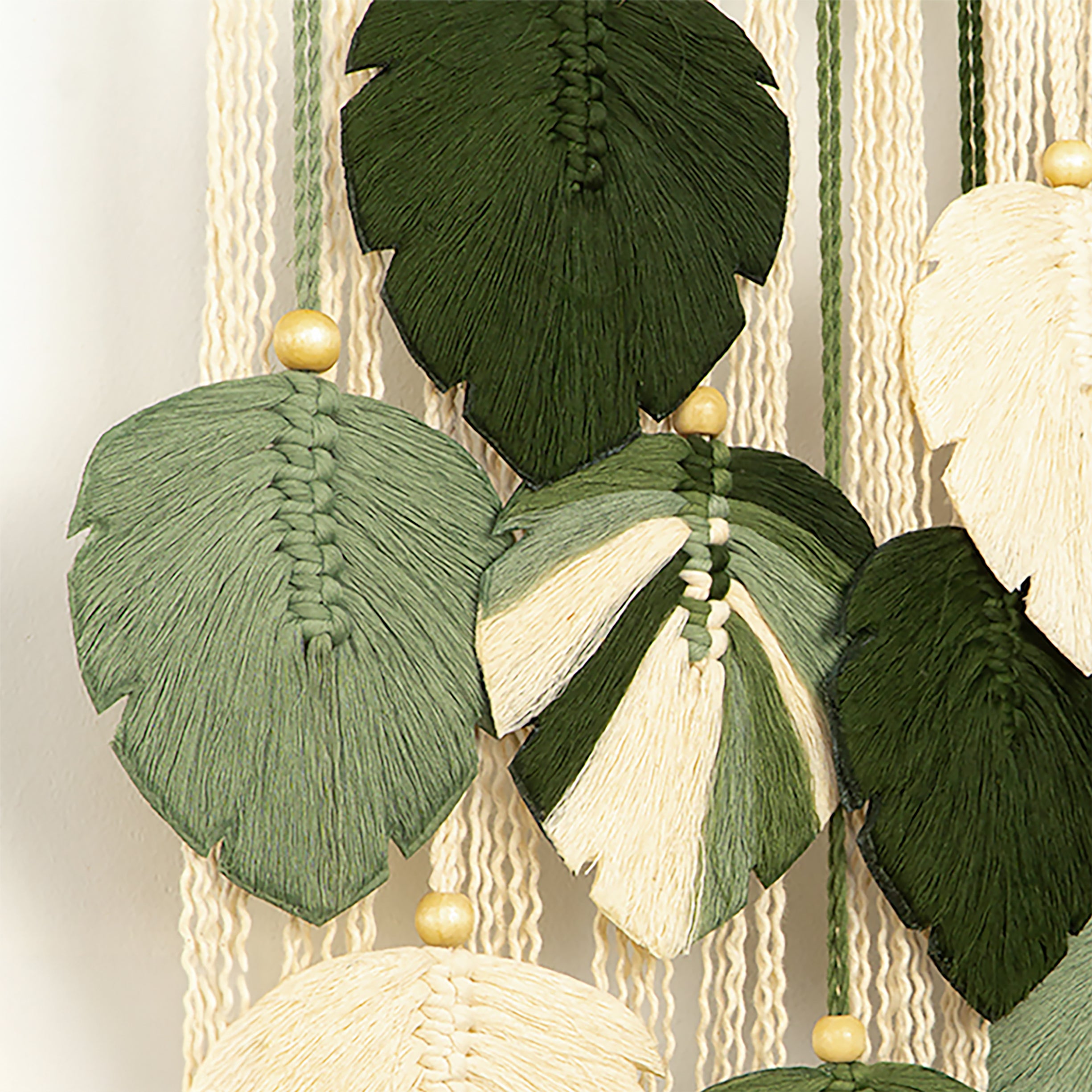 Decorative wall hanging with leaf-shaped tassels on a textured wall.