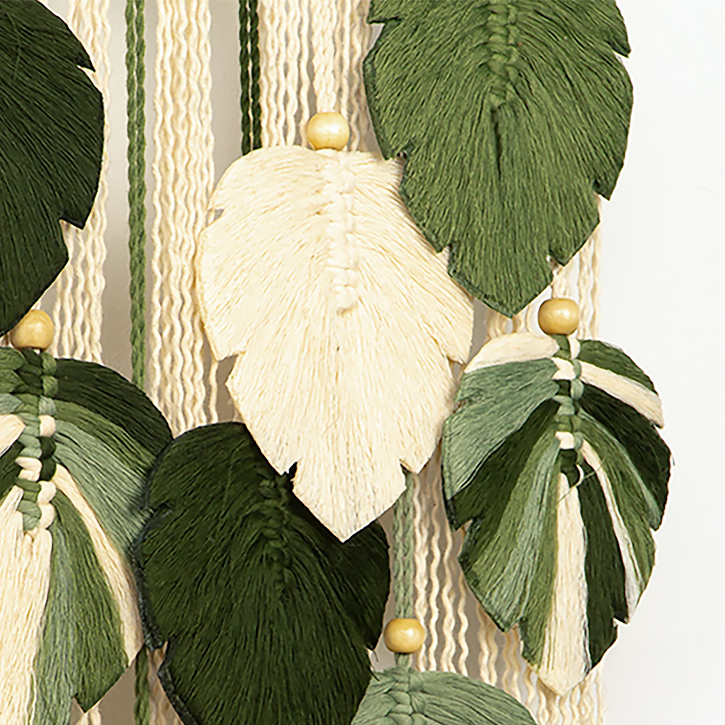 Decorative wall art with green and cream leaves and wooden beads on a textured background