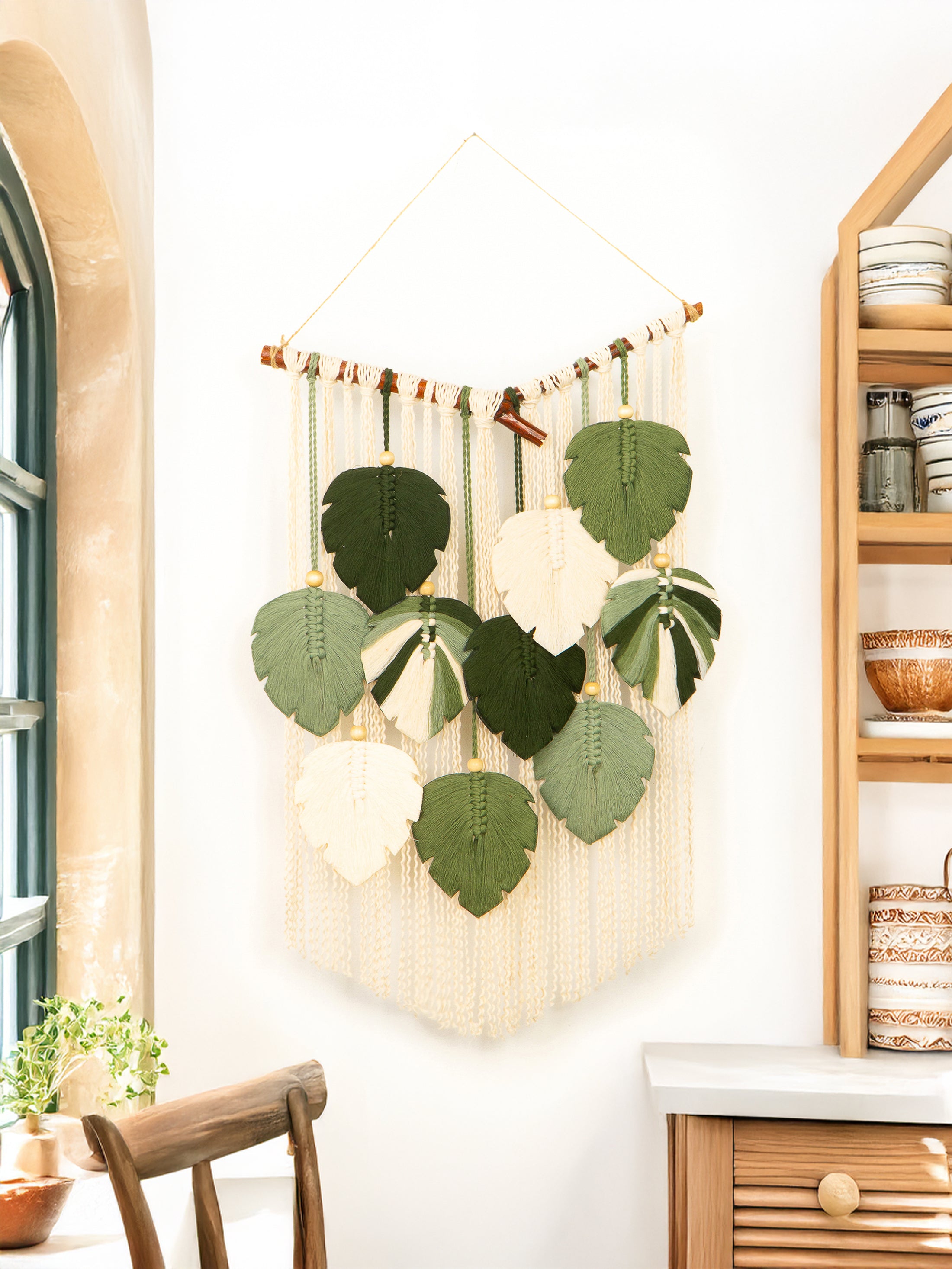 Decorative wall hanging with green leaf-shaped elements on a white wall.