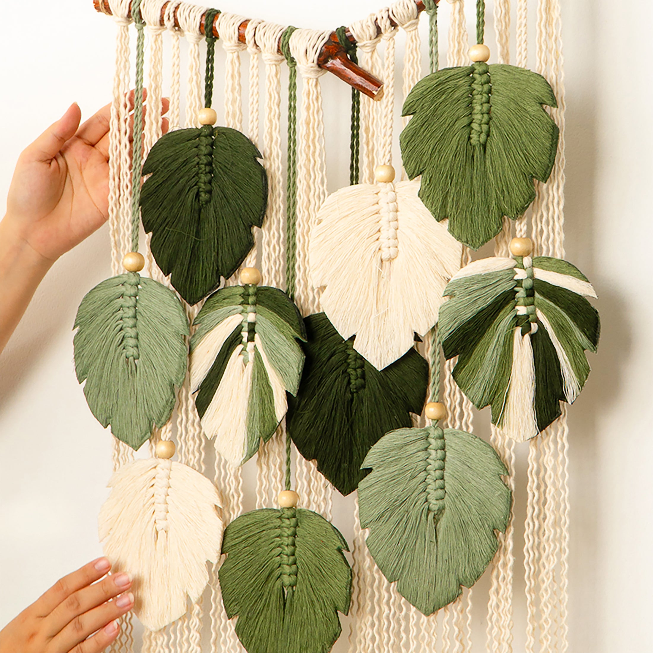 Macrame wall hanging with leaf-shaped decorations on a plain background