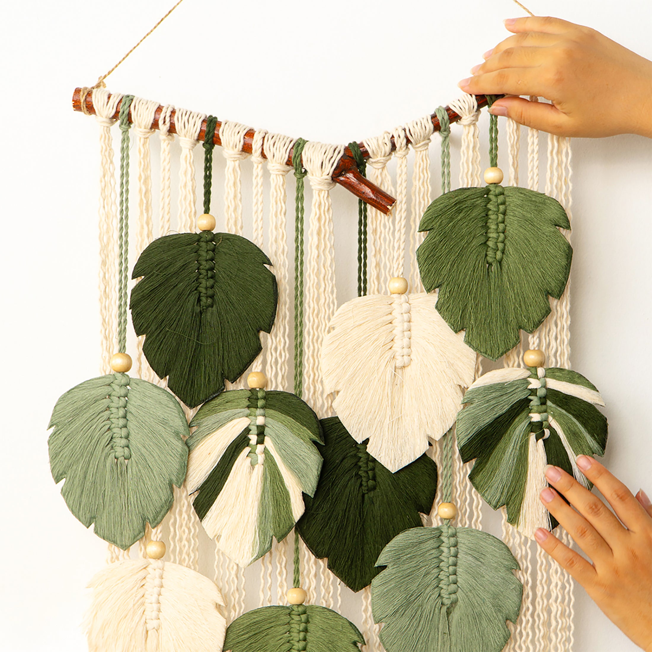 Decorative wall hanging with leaf-shaped tassels and hands adjusting it.