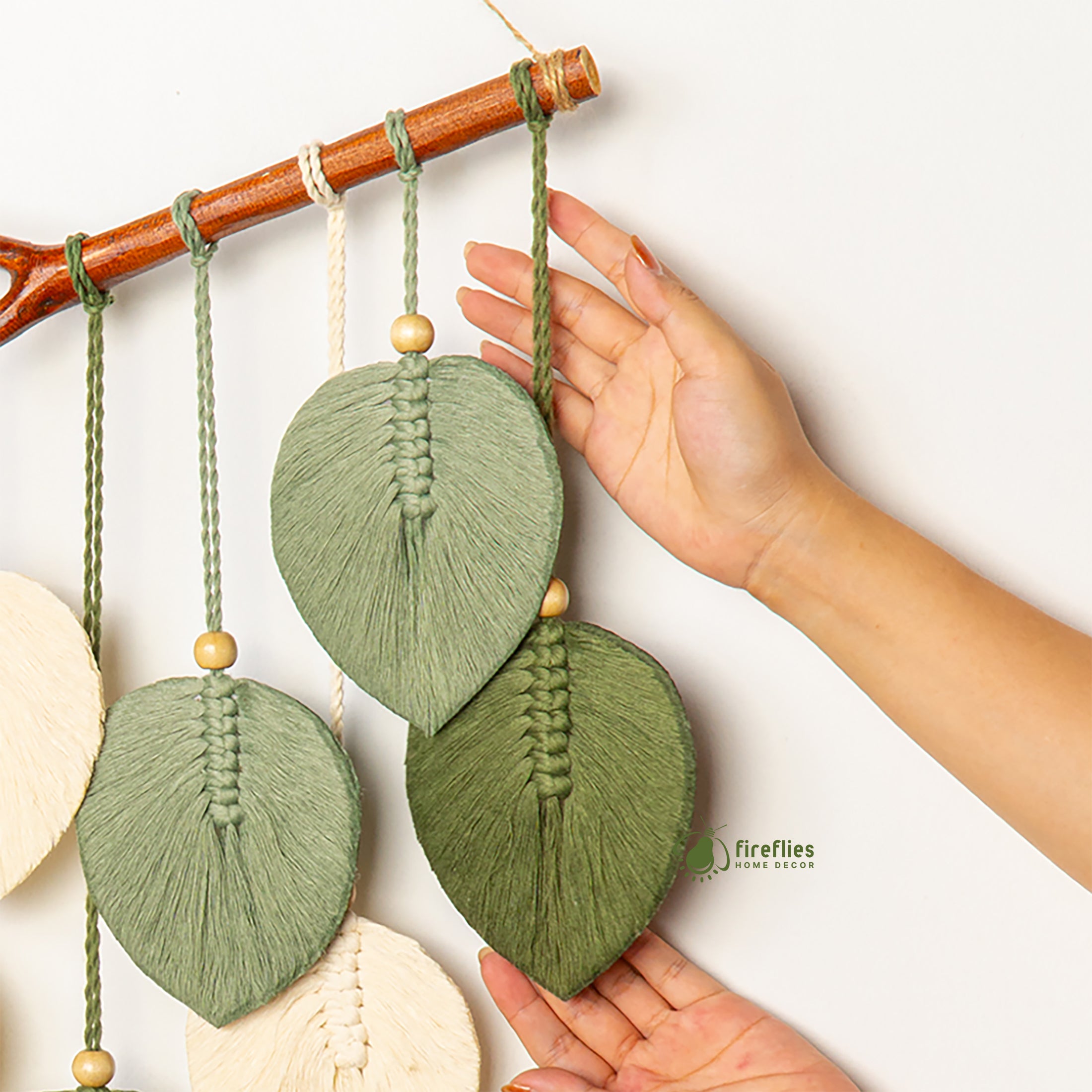 Handmade leaf-shaped decorations hanging from a branch with a visible brand logo.