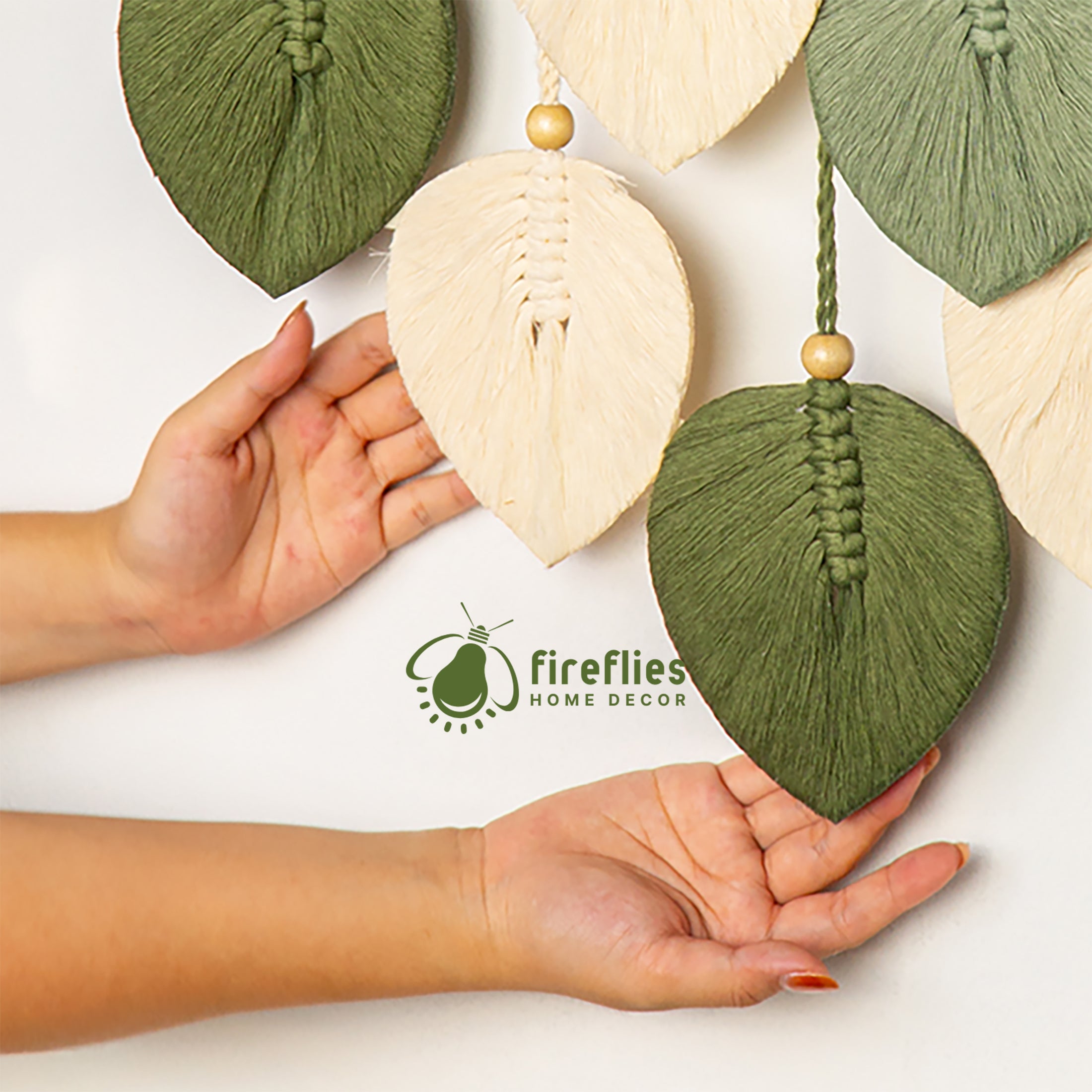 Decorative wall hanging with hands holding it, featuring the Fireflies Home Decor logo.