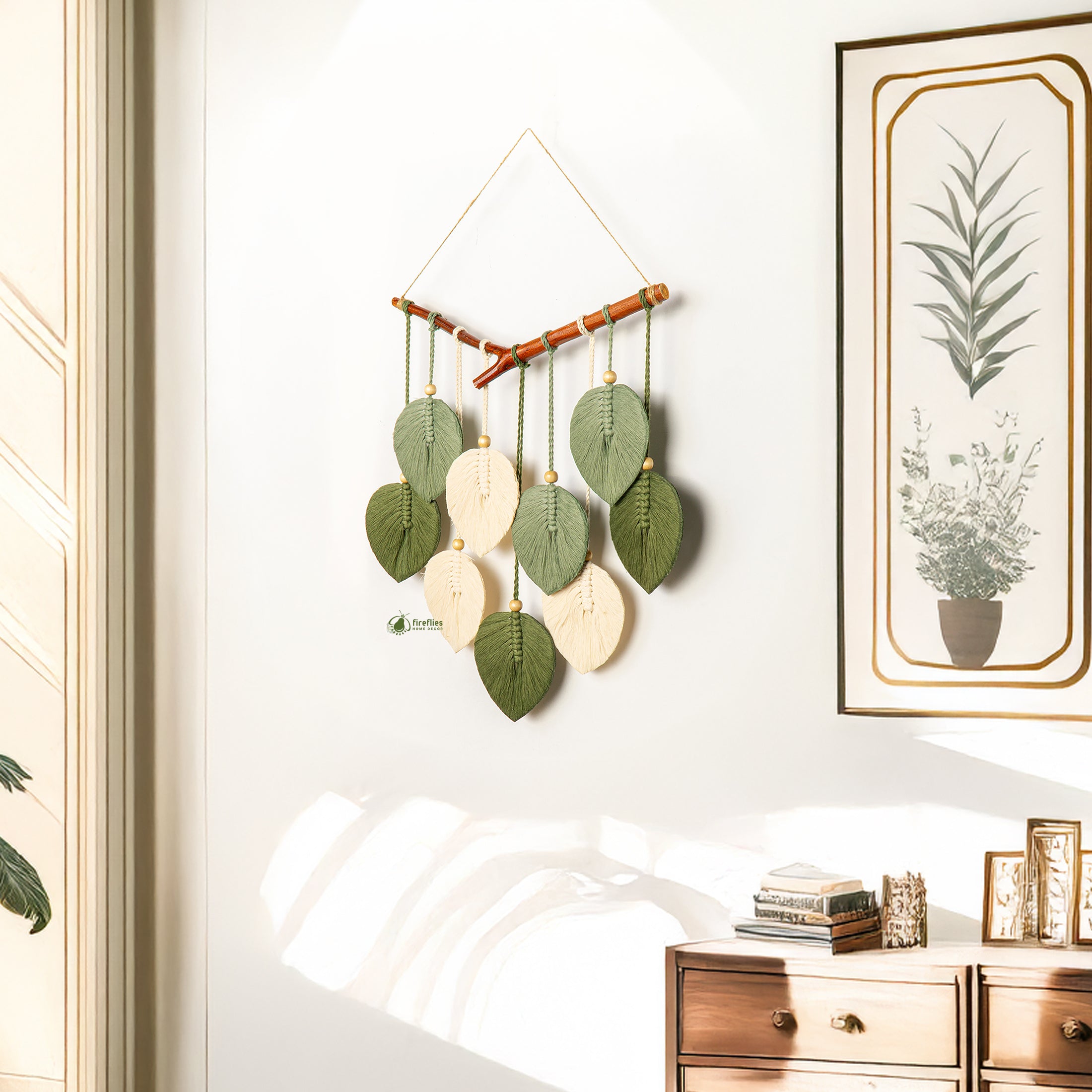 Decorative wall hanging with leaf-shaped beads on a white wall with a framed picture of a plant.